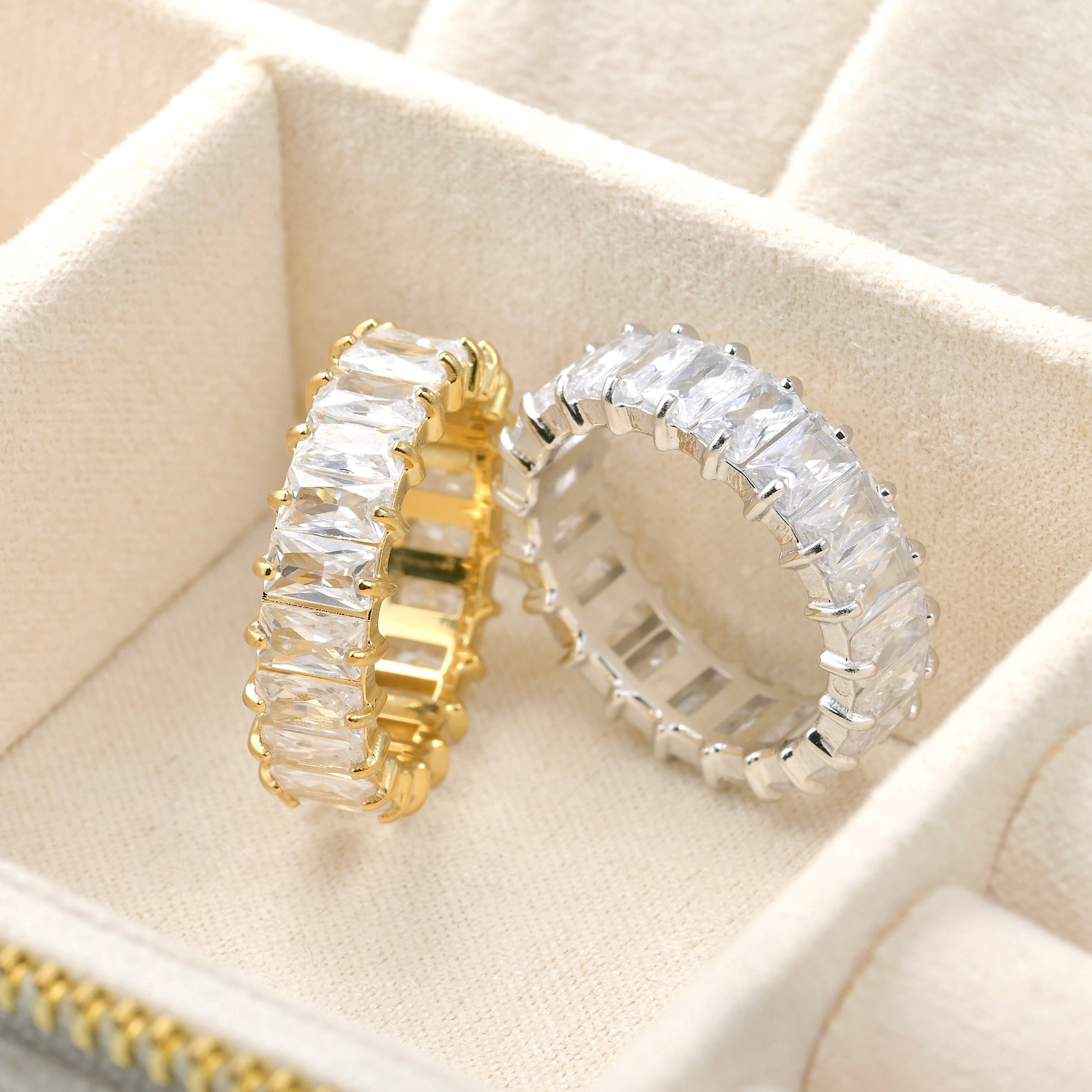 Gold and silver eternity rings with clear gemstones on a beige jewelry box.
