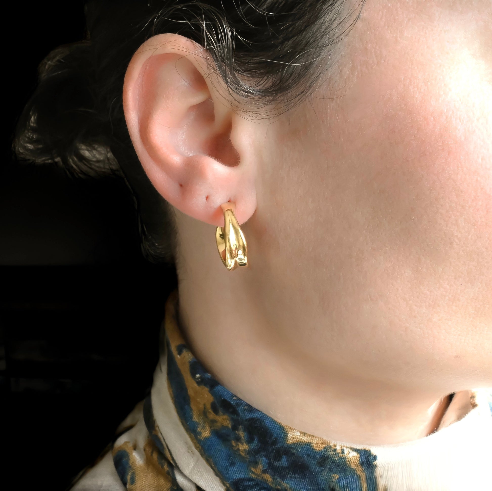 Gold molten hoop earring worn by a person with a dark background