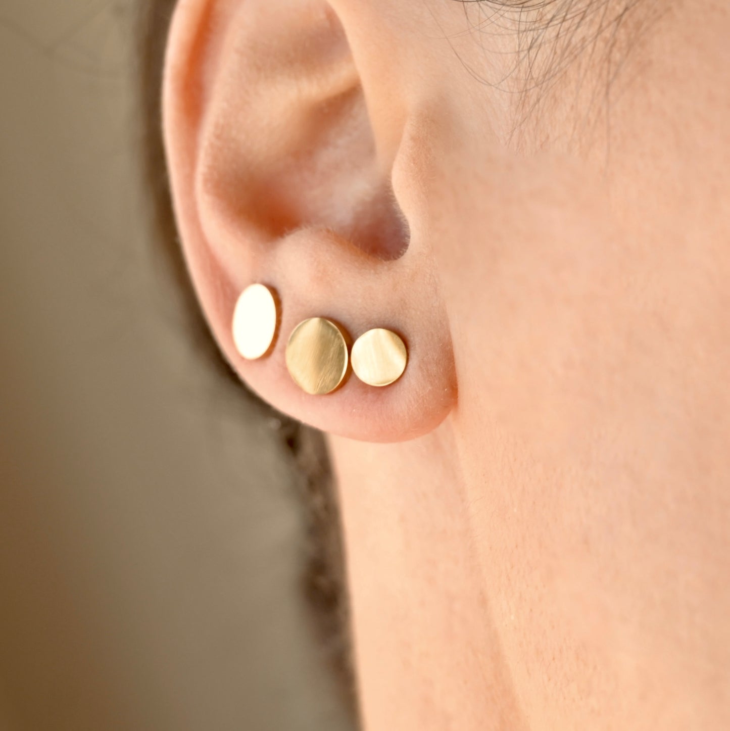 Close-up of an ear wearing three gold circle earrings in 6mm, 8mm and 10mm, against a neutral background