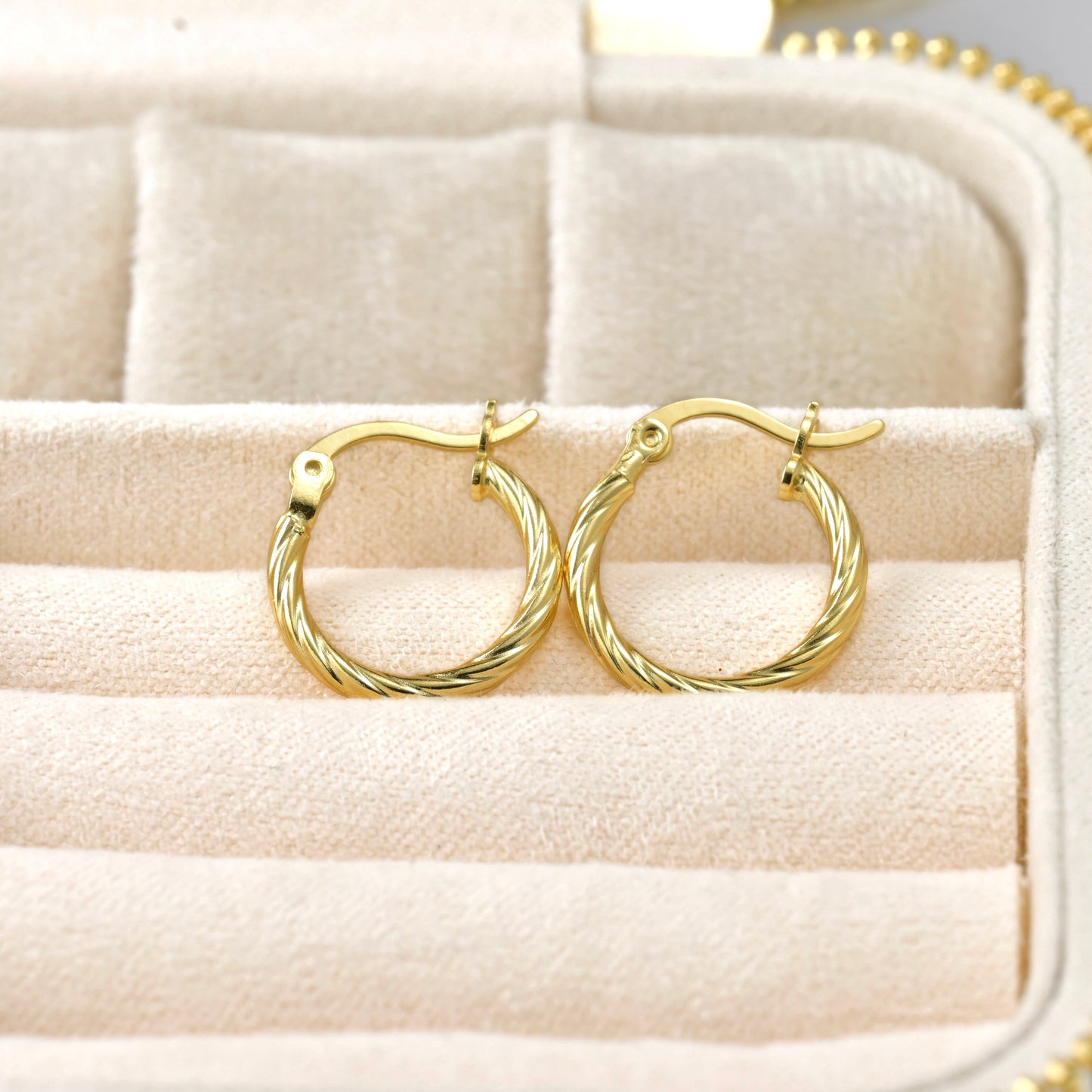 18k Gold thin hoop earrings on a textured beige surface