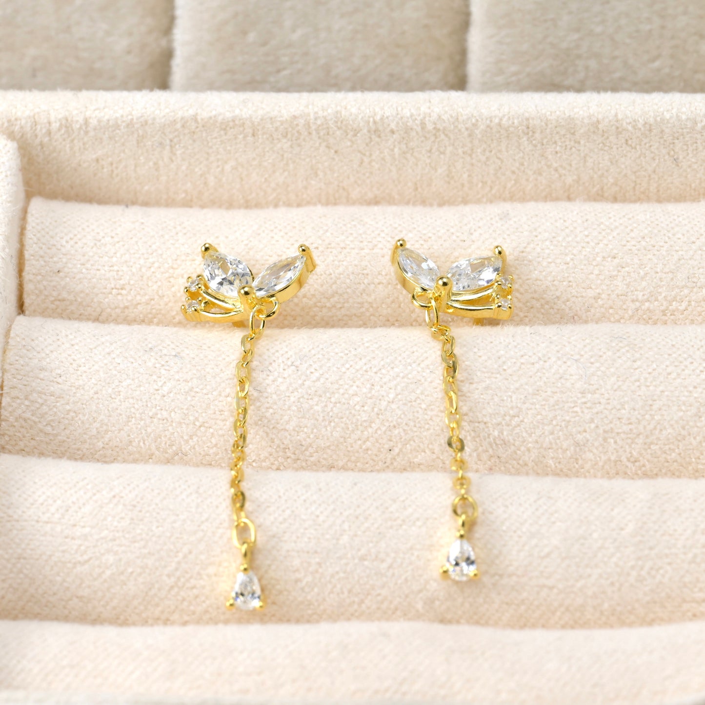 Dainty Gold earrings with clear gemstones on a beige cushion
