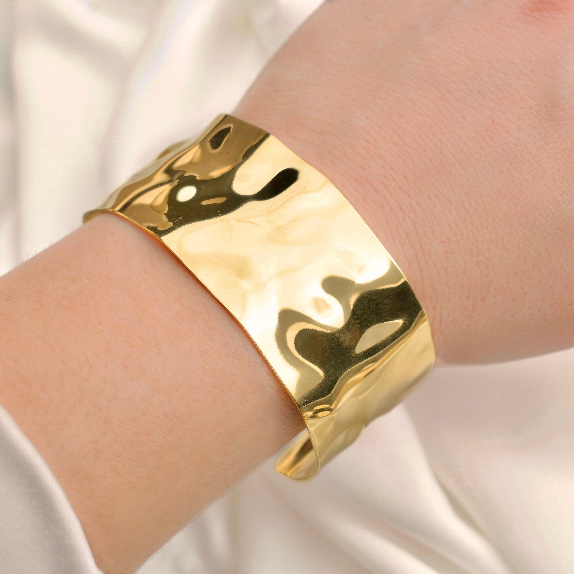 Chunky gold bracelet on a wrist with a plain background