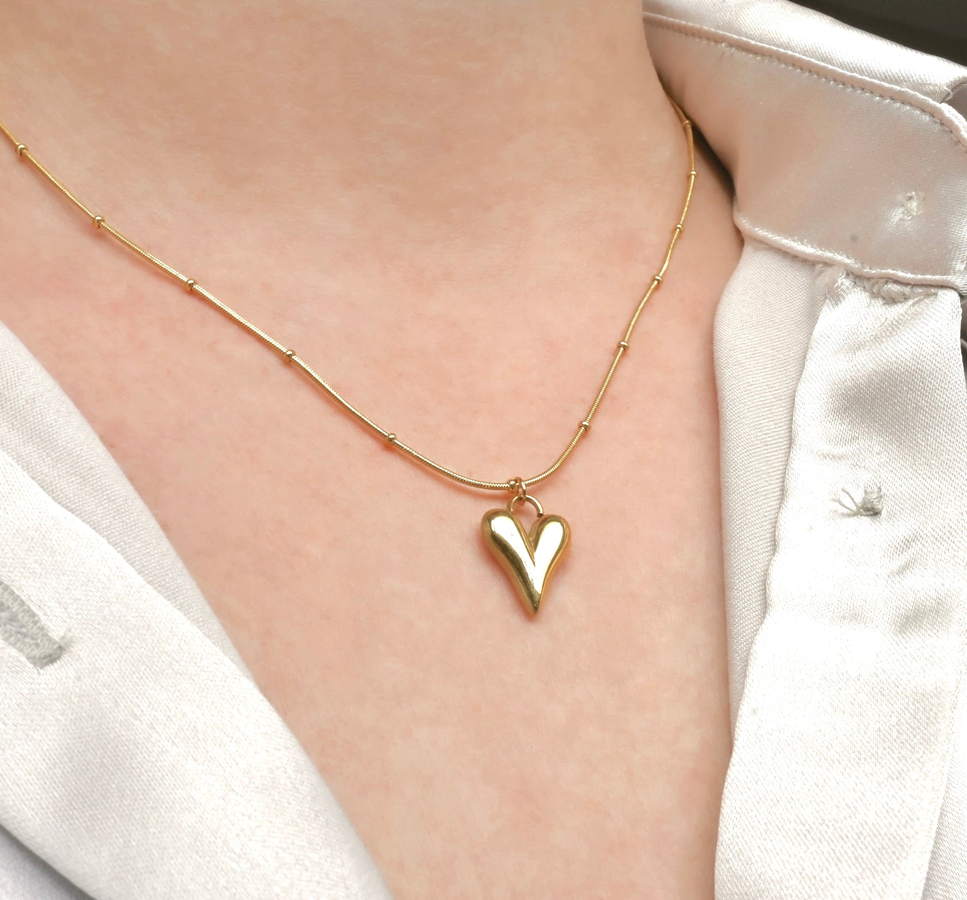 Gold heart necklace on a person wearing a white shirt