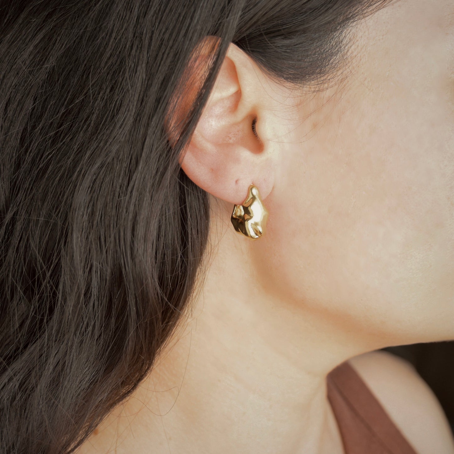 Close-up of a person wearing a gold earring with dark hair.
