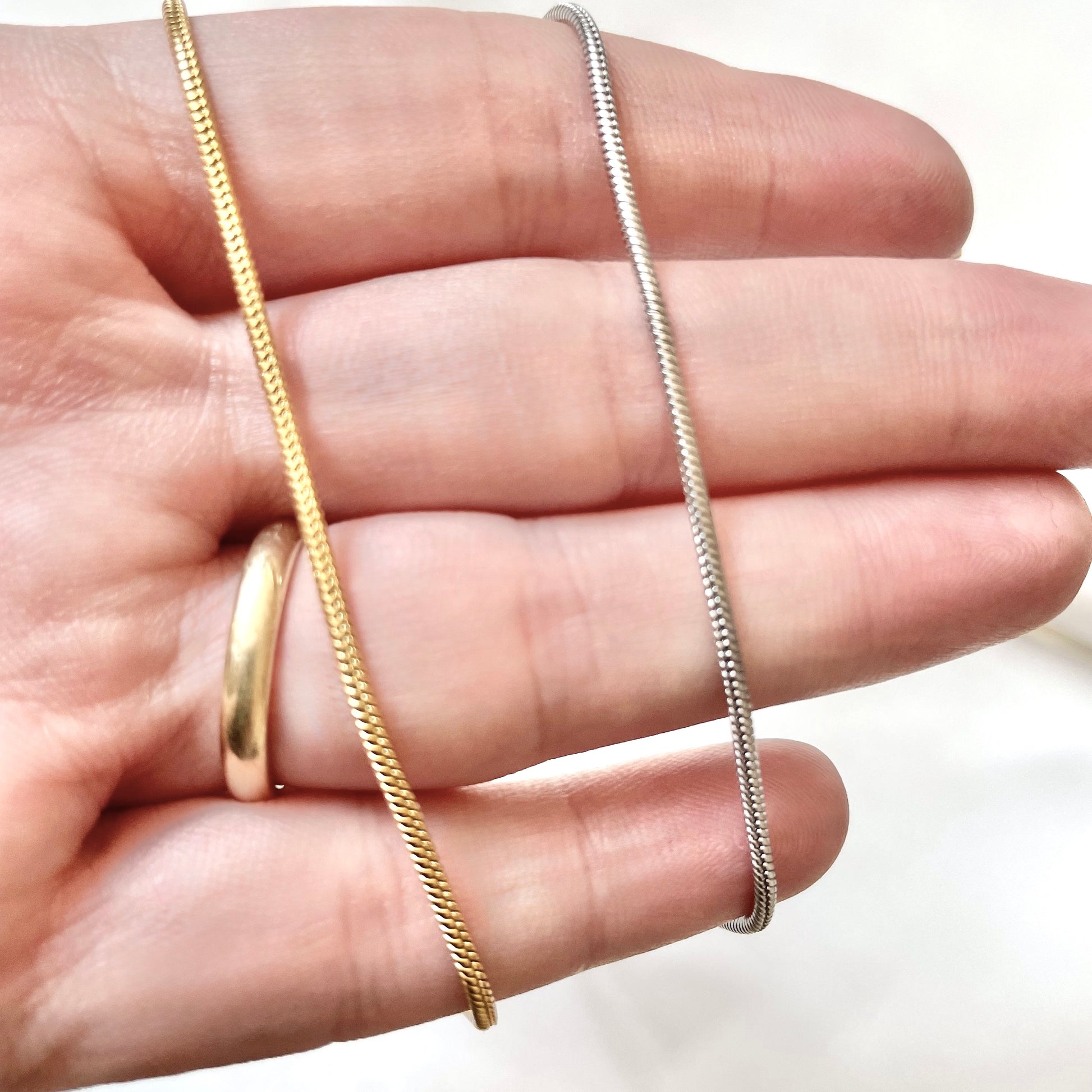 Gold and silver skinny snake chains on a hand against a white background