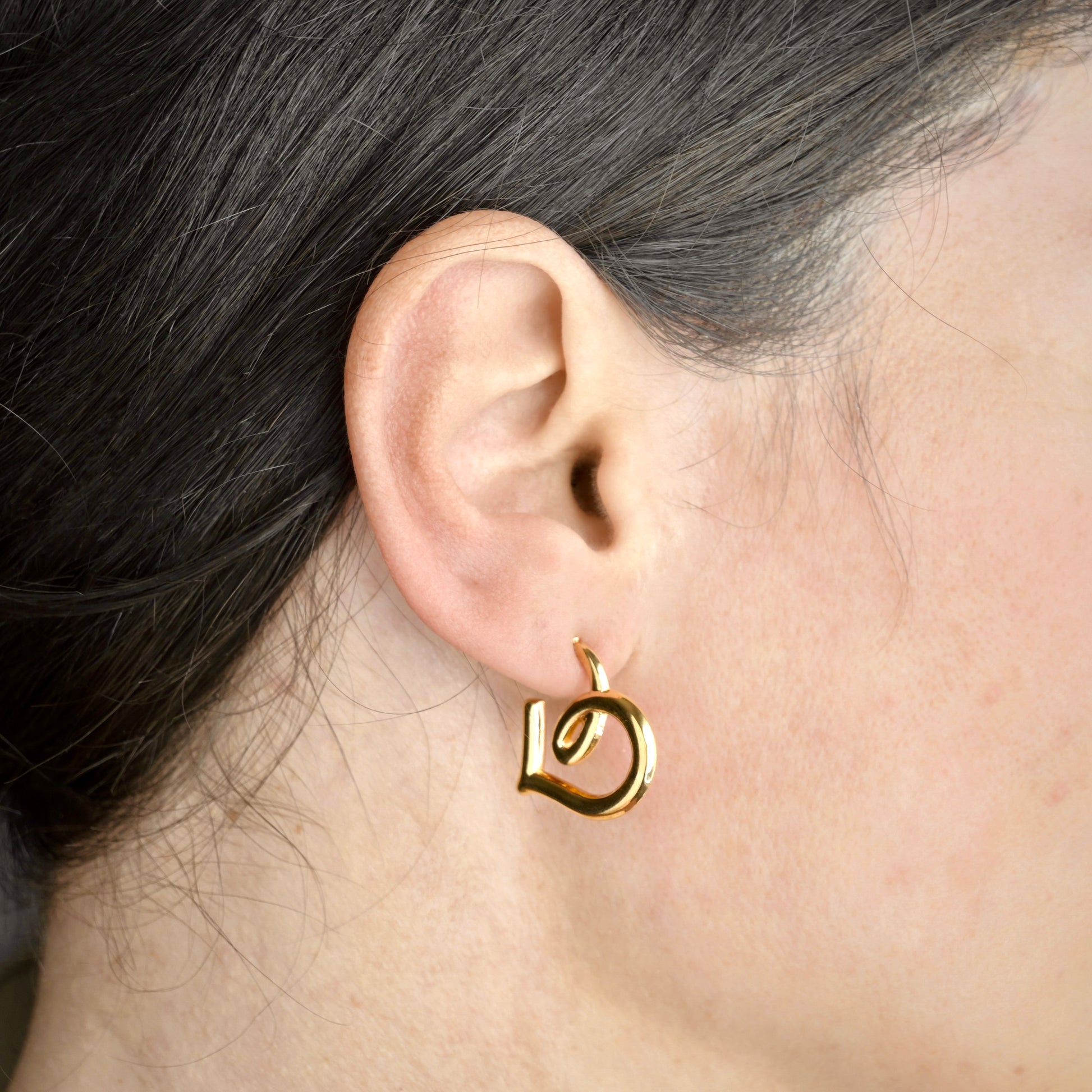 Gold swirl heart earring worn on an ear with a close-up view