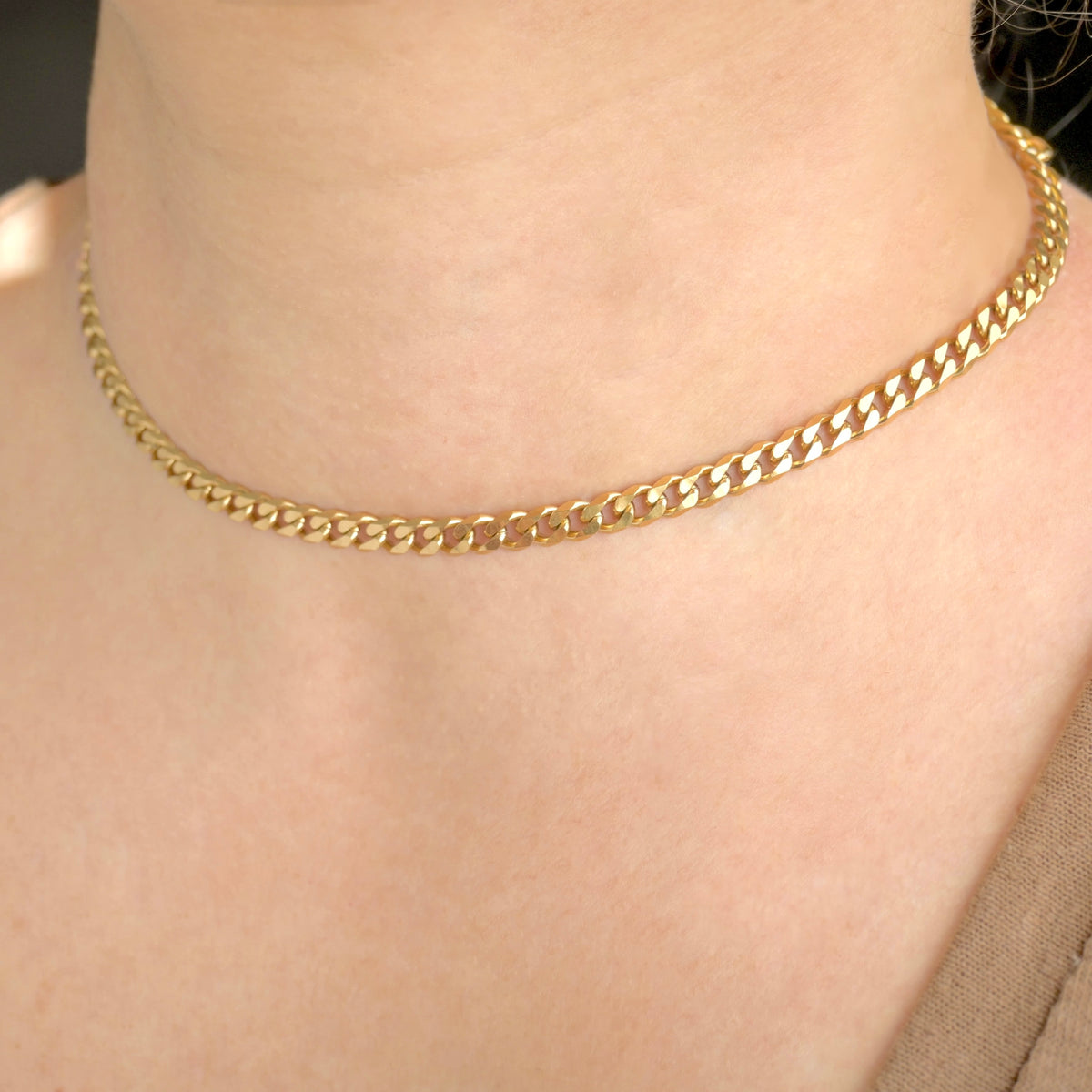 A close-up of a person's neck and upper chest wearing a thick yellow gold cuban chain necklace.