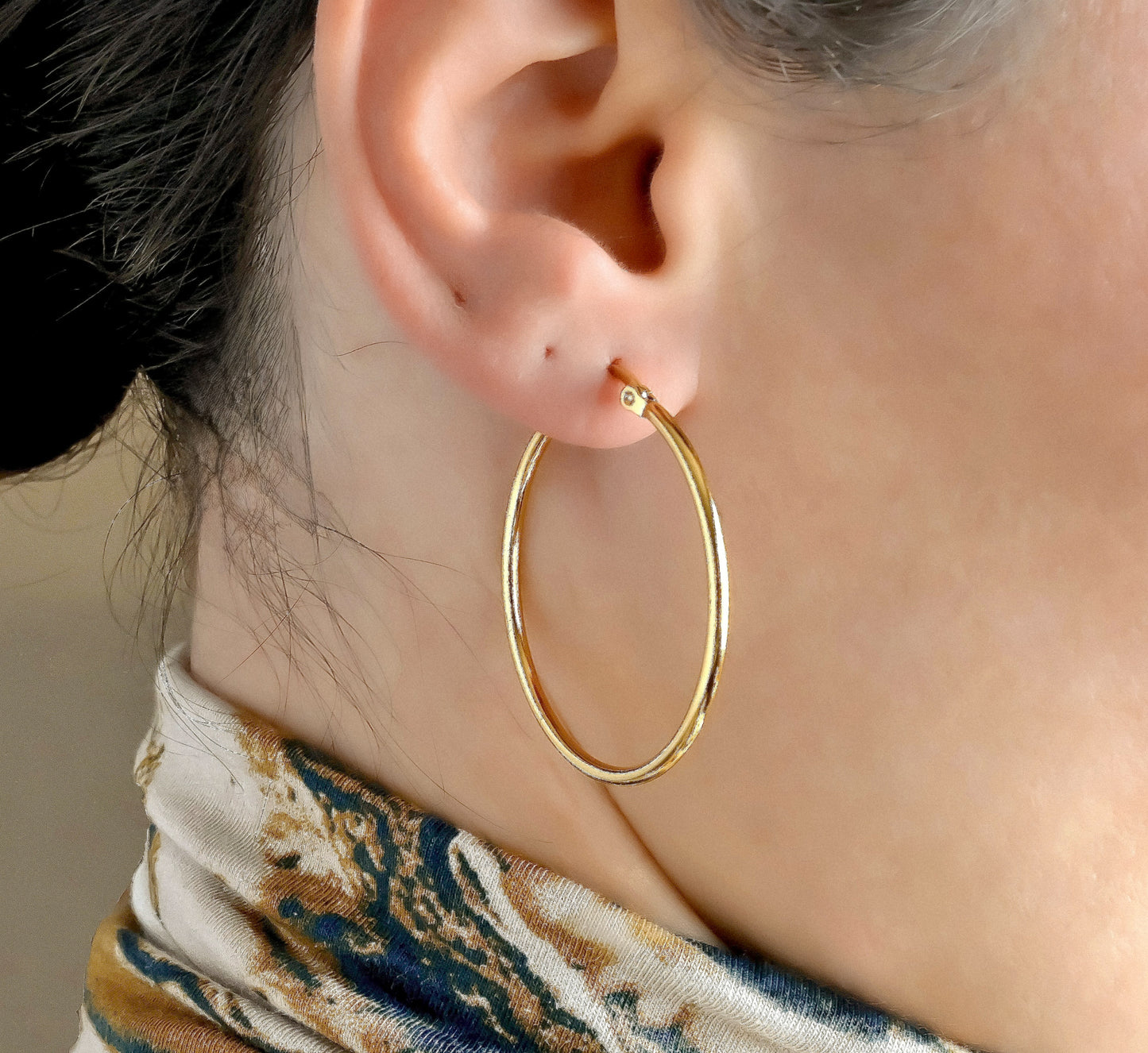 40mm Gold hoop earrings worn by a person with a blurred background
