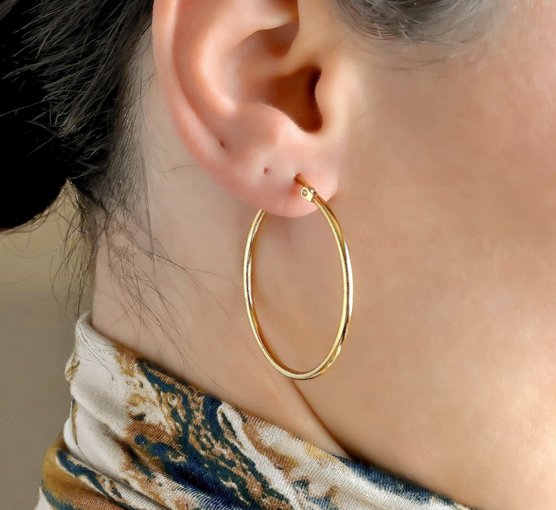 40mm Gold hoop earrings worn by a person with a blurred background