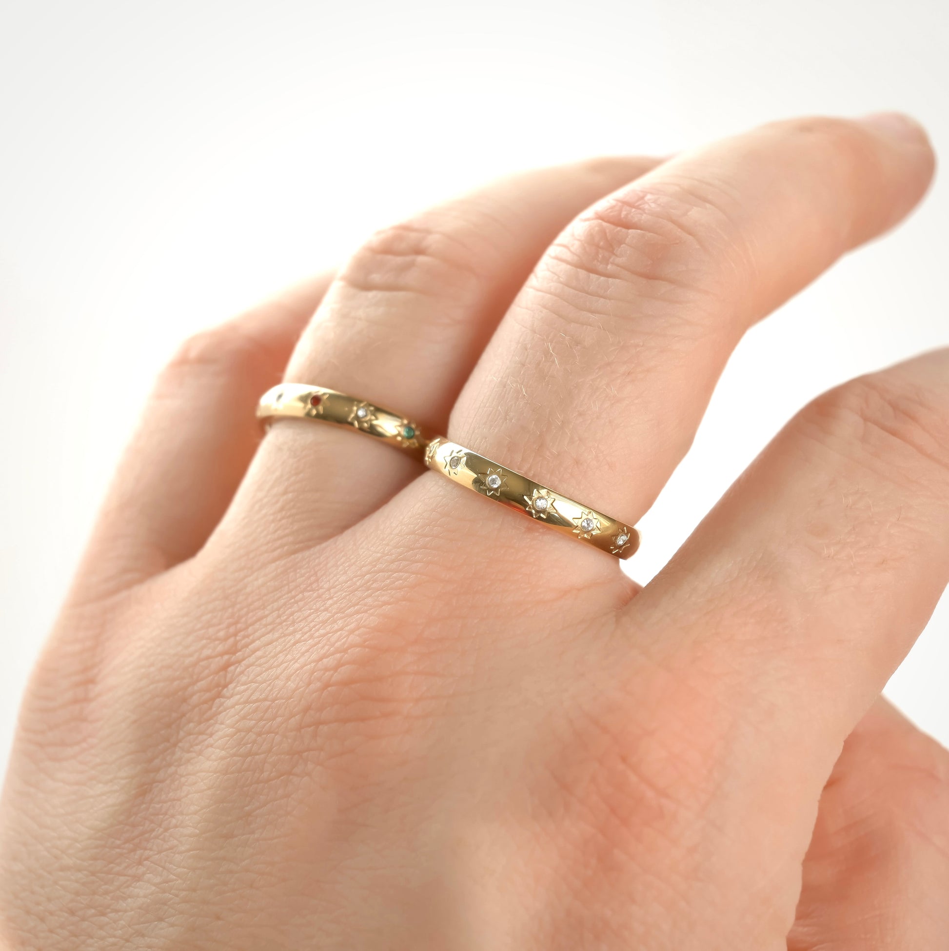 Close up of hand wearing two gold star rings with clear and mixed color diamonds