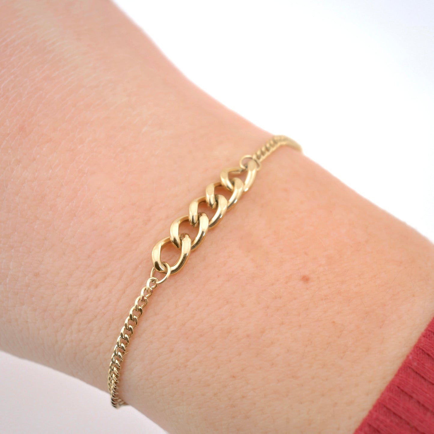 Gold cuban chain bracelet on a wrist with a plain background