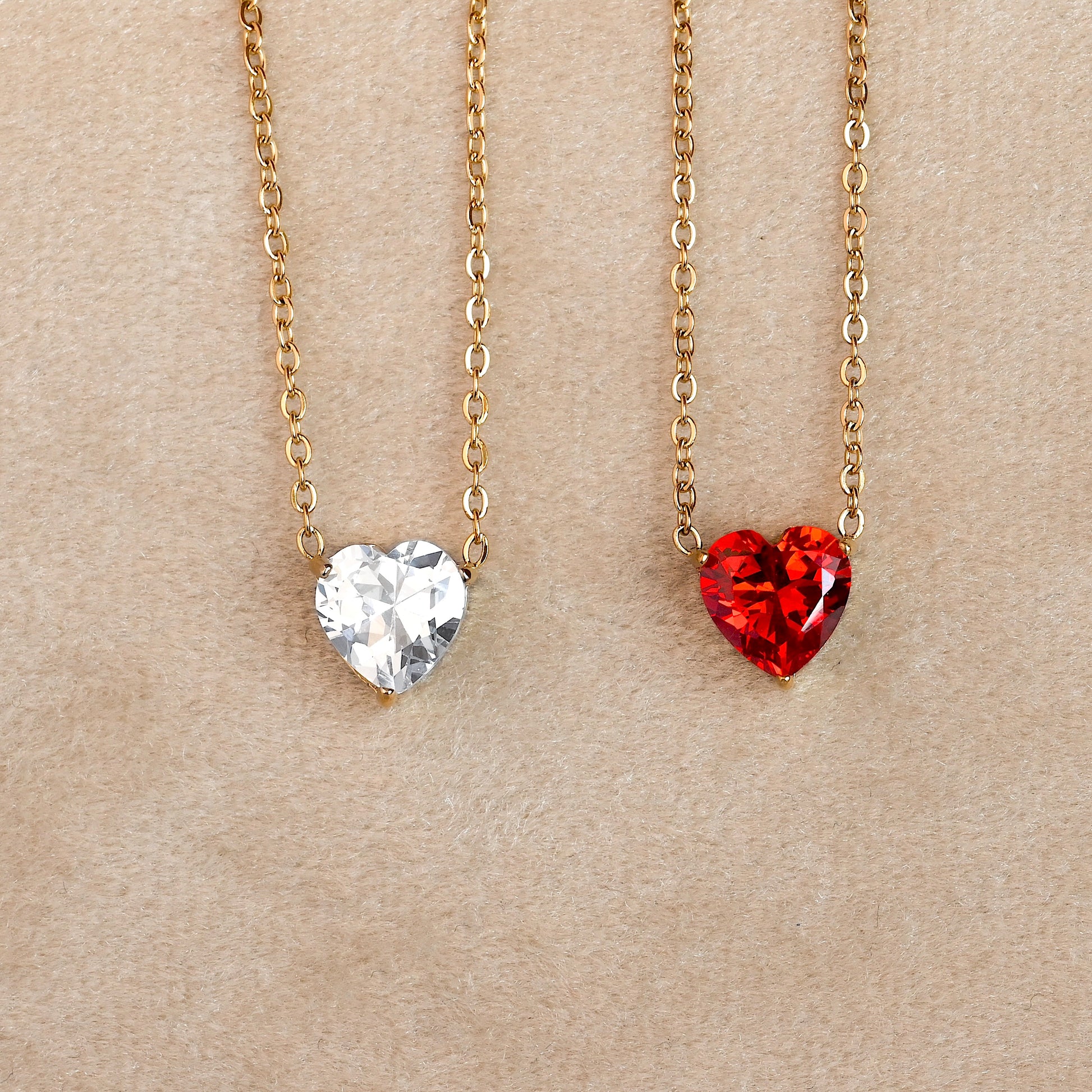 Two heart-shaped pendants with red and white stones on gold chains against a beige background