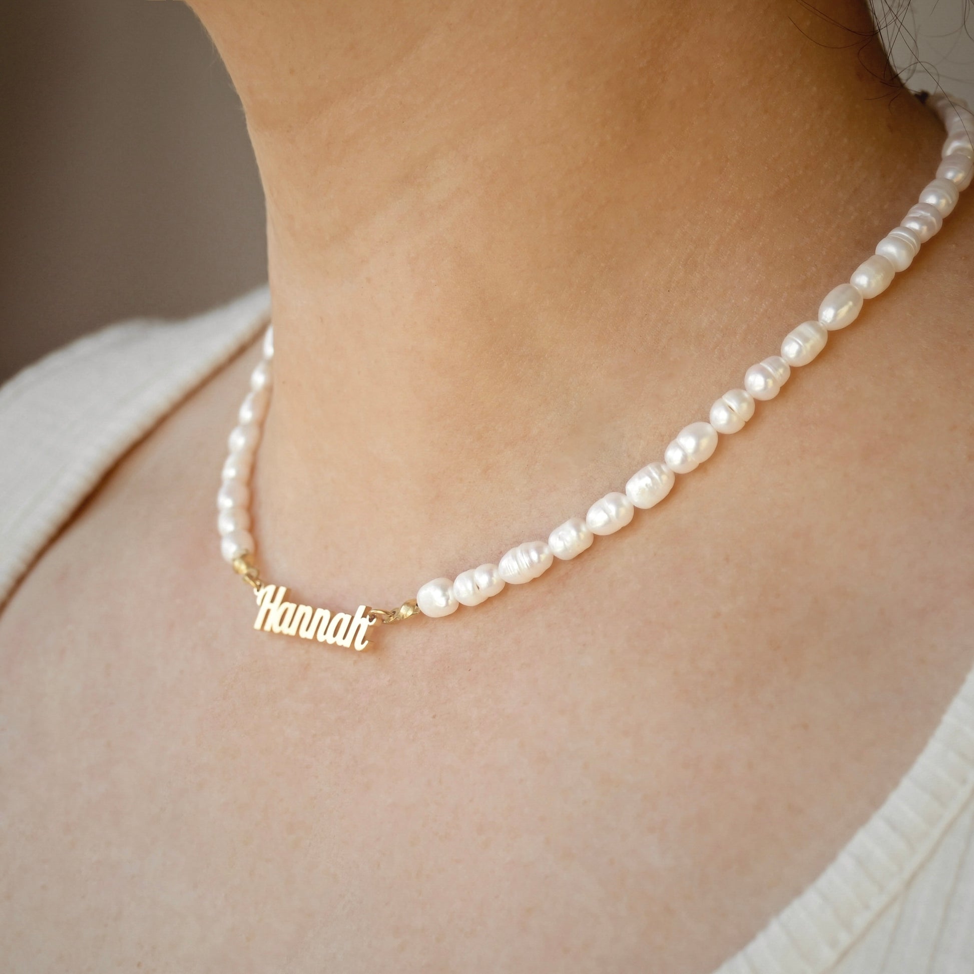 Pearl necklace with a gold name pendant on a person wearing a white top.