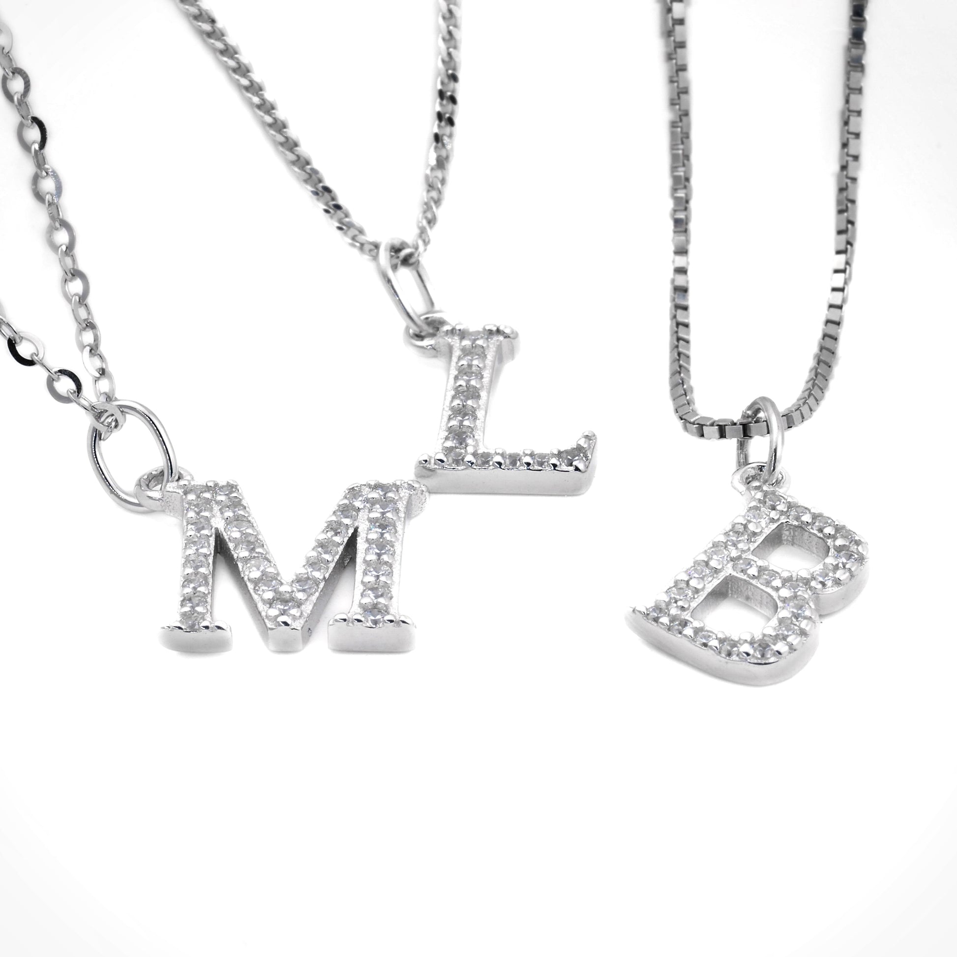 Three silver letter necklaces with 'M', 'L' and 'B' pendants on a white background