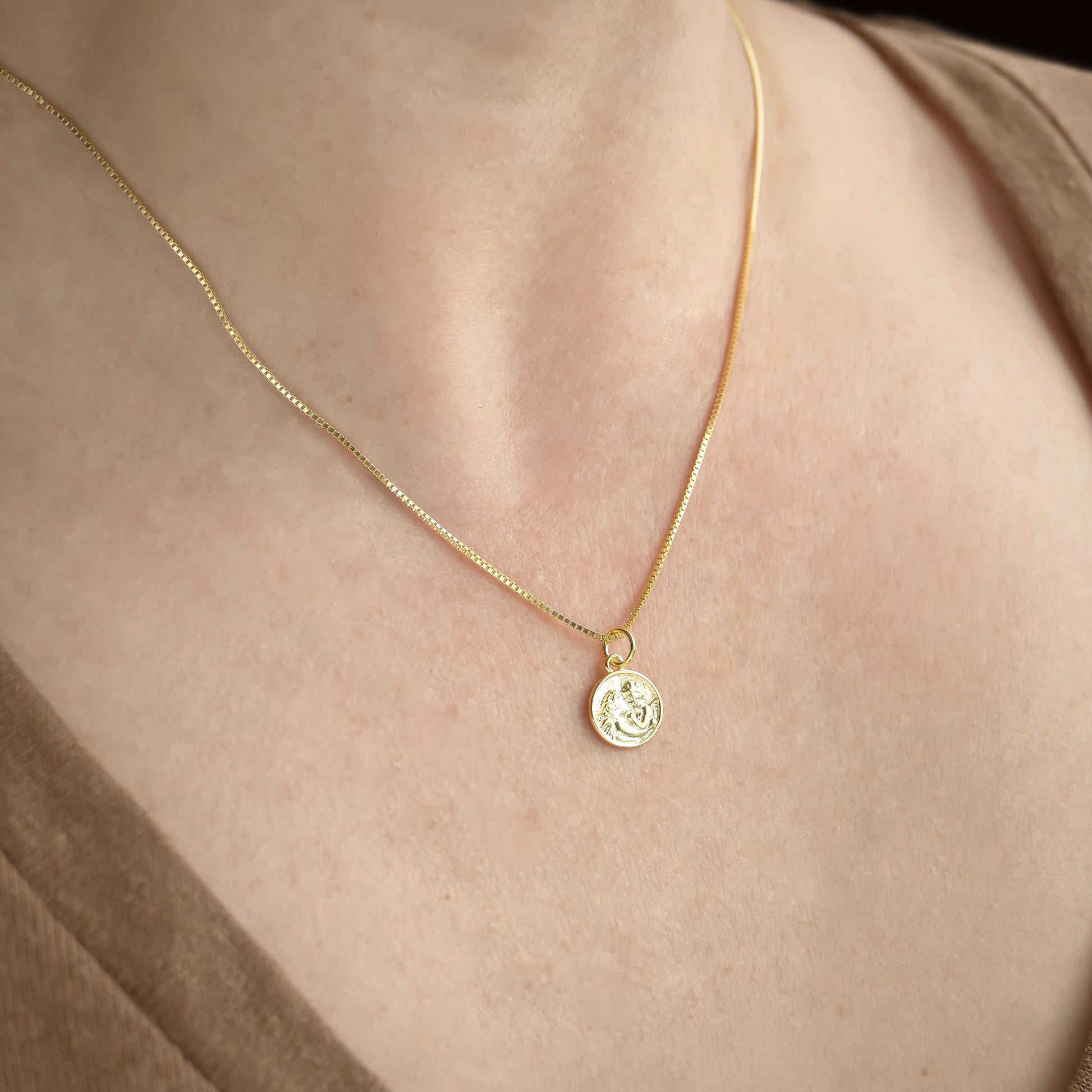 Gold box chain necklace with a coin pendant on a person's neck