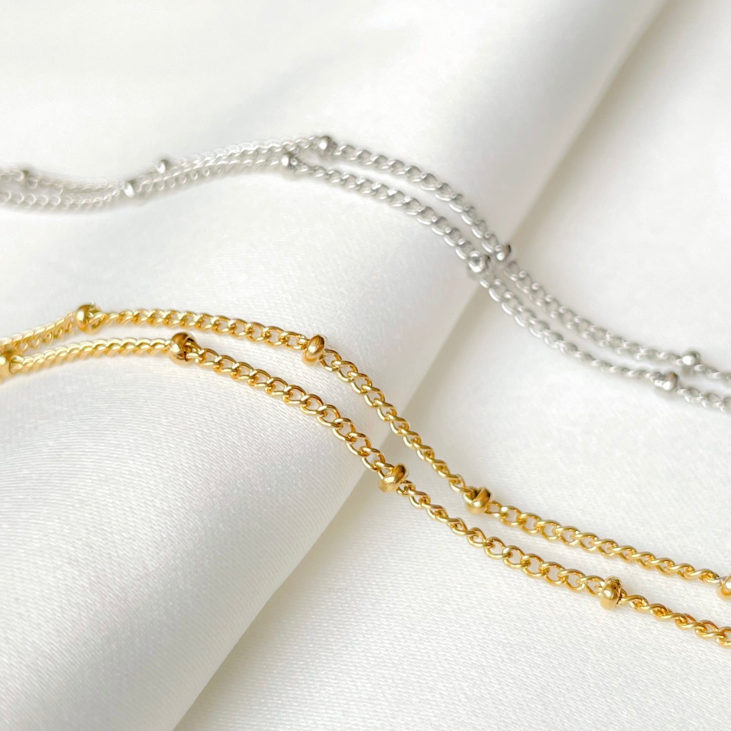 Two-layered gold and silver bracelets on a white fabric background