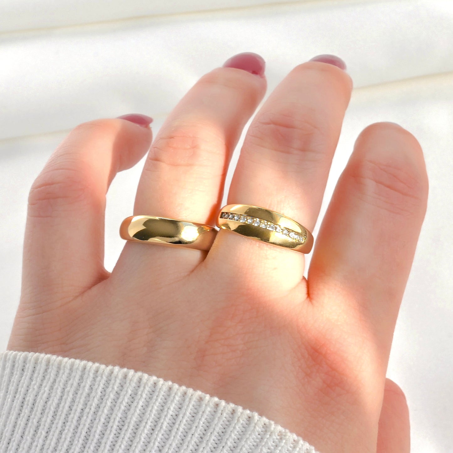 Hand wearing two gold rings, one plain and one cz line dome rings side by side on a light background