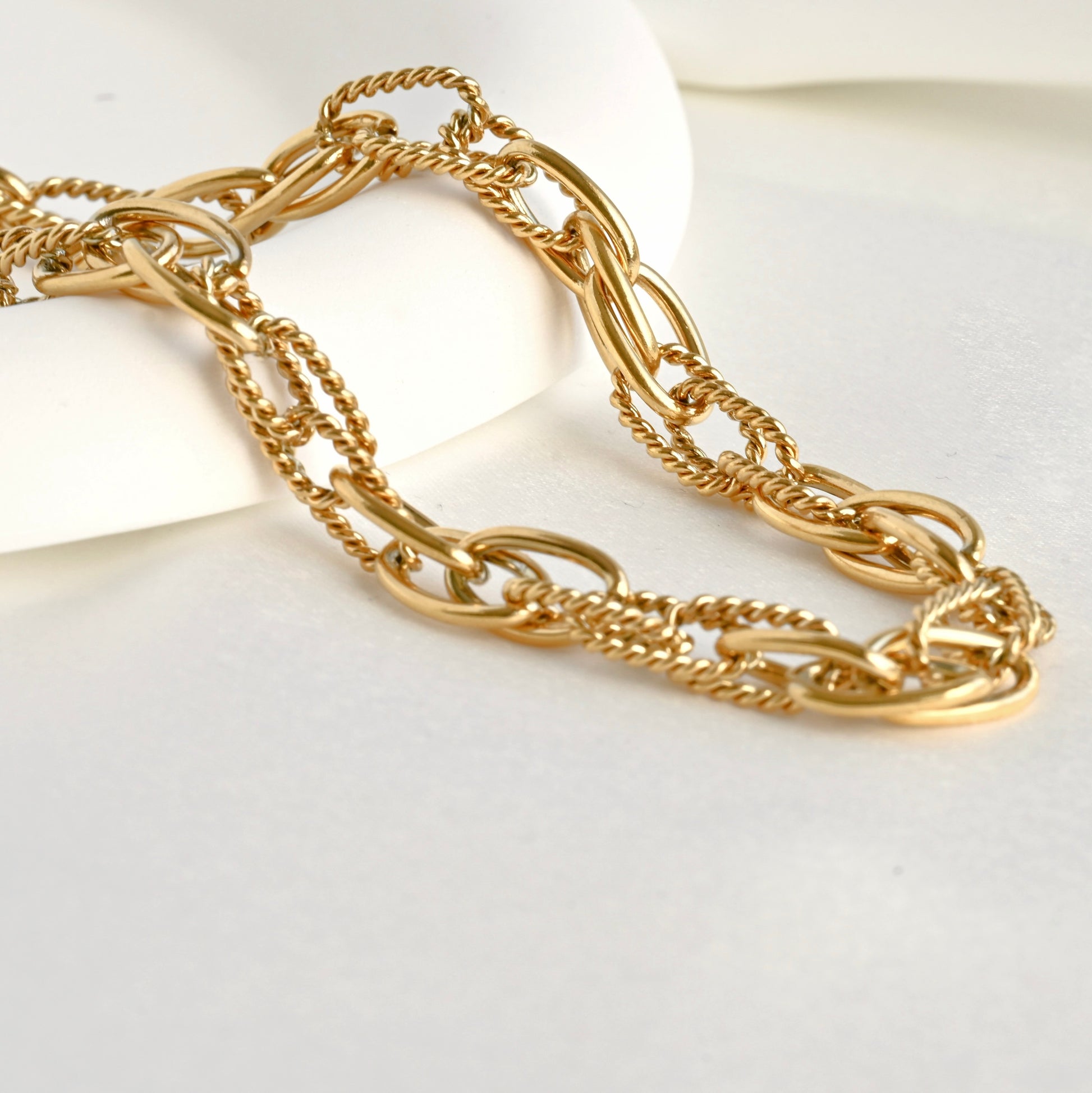 Gold mixed oval link chain bracelet on a white plate