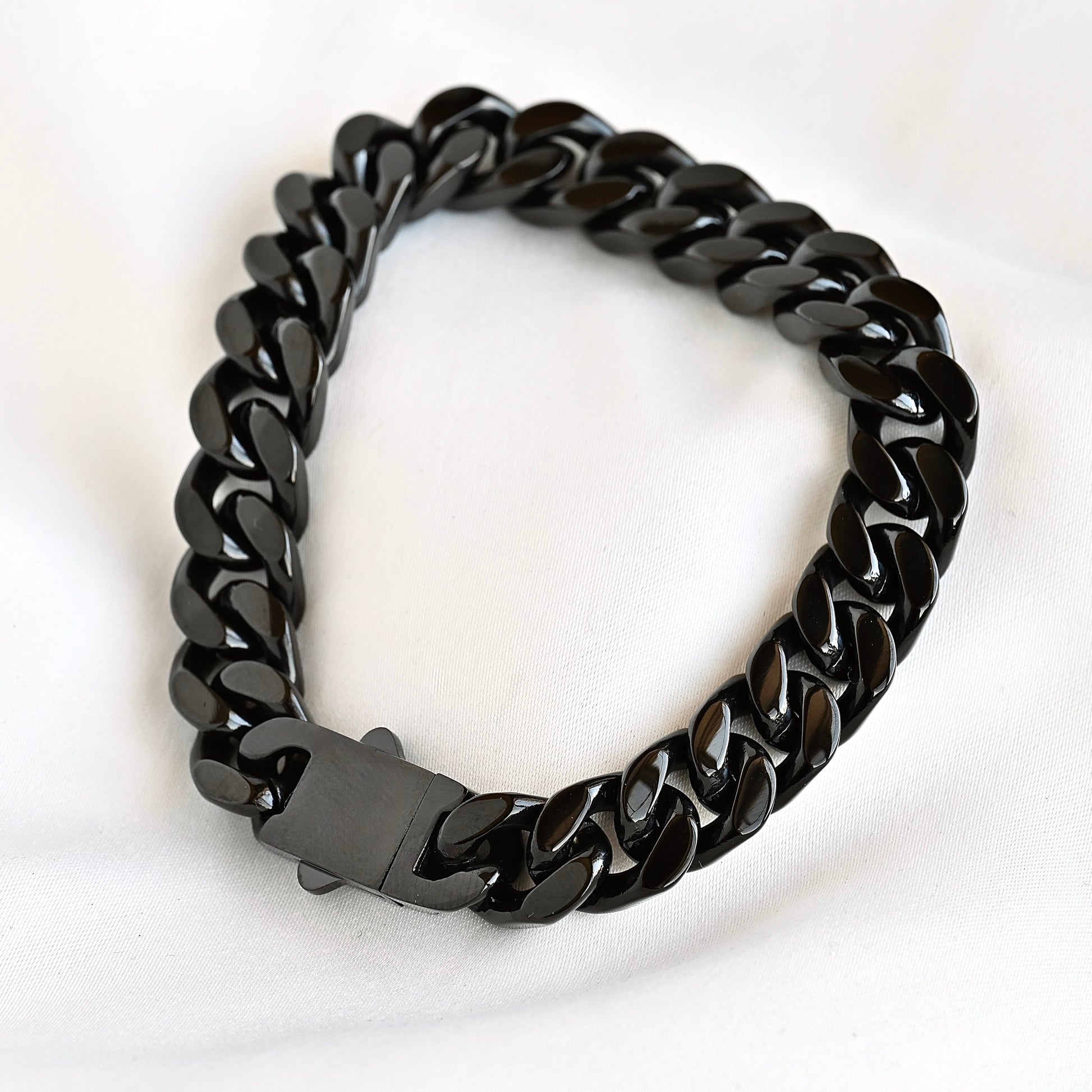 A glossy black Cuban link chain bracelet with a matching black box clasp, displayed on a soft white fabric background.