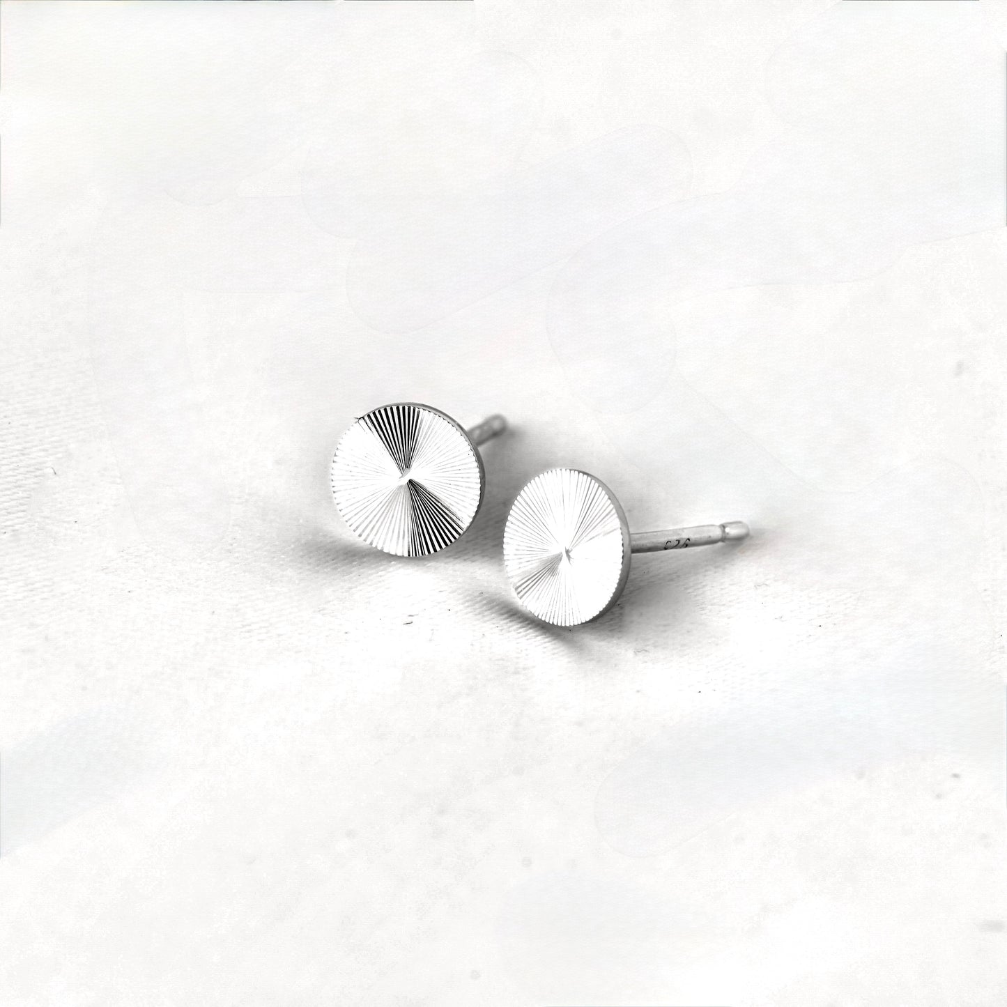 Pair of tiny silver starburst earrings on a light gray background
