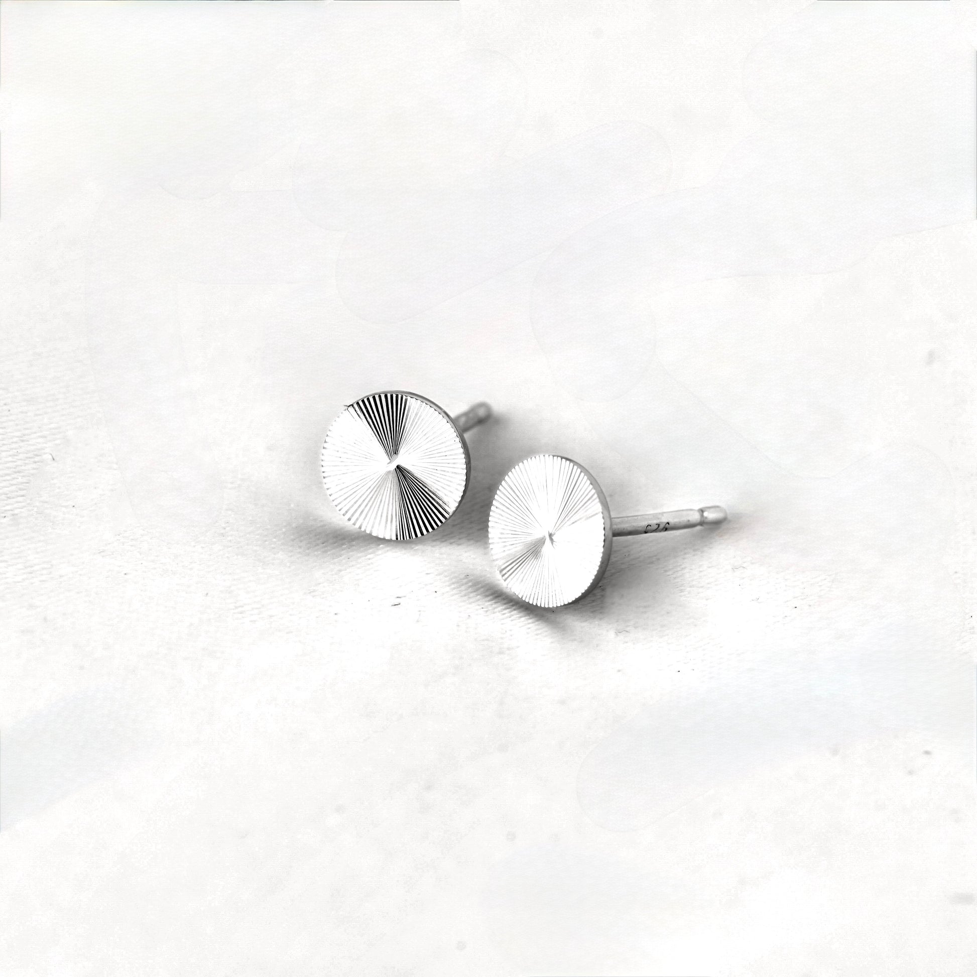 Pair of tiny silver starburst earrings on a light gray background