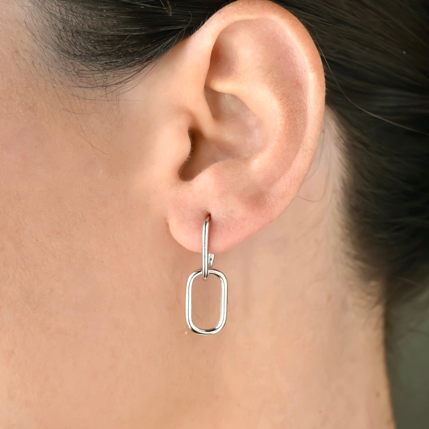 Close-up of an ear wearing a silver U link hoop earring with a blurred background