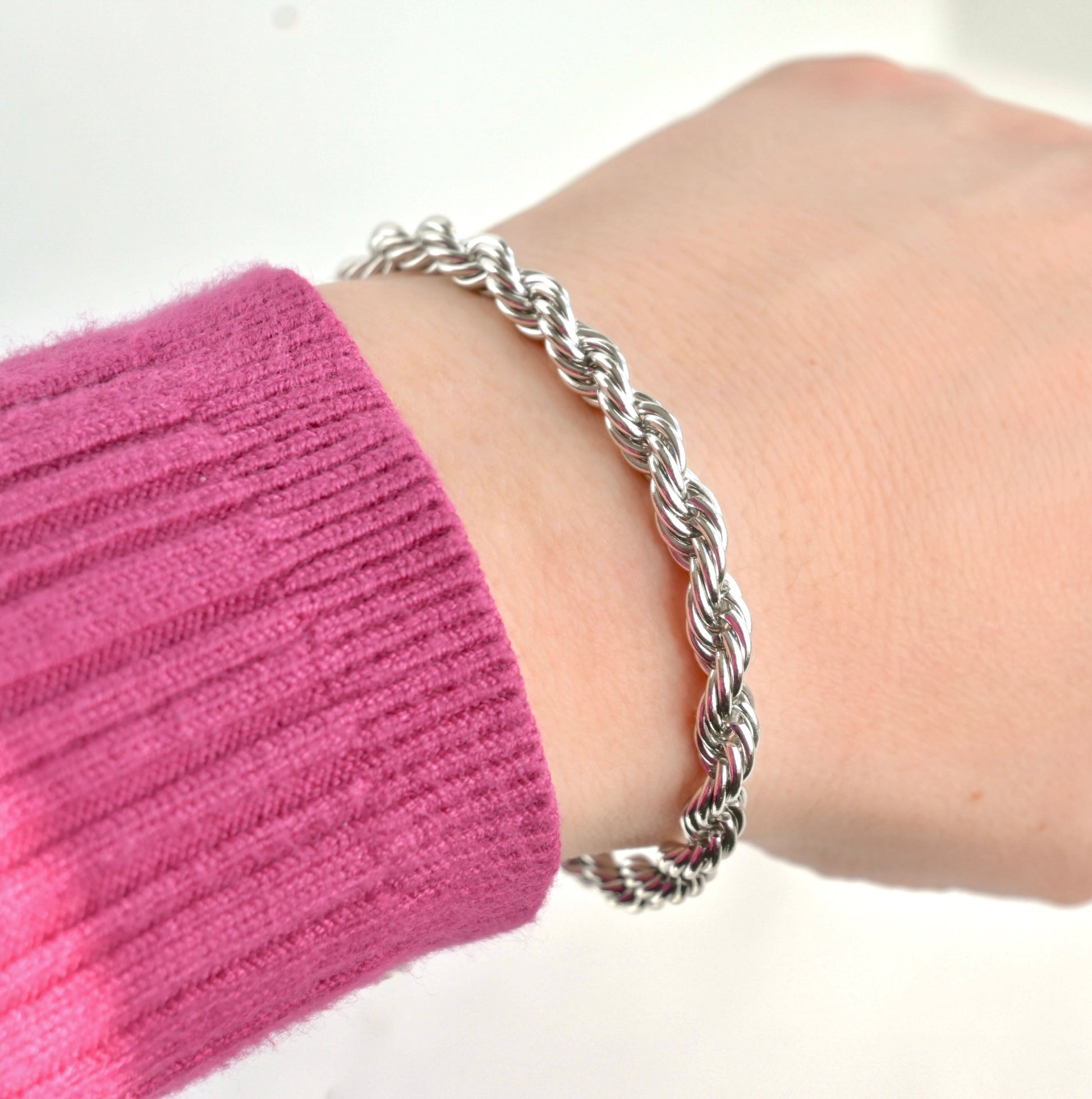 Silver thick rope bracelet on a wrist with a pink sleeve against a white background