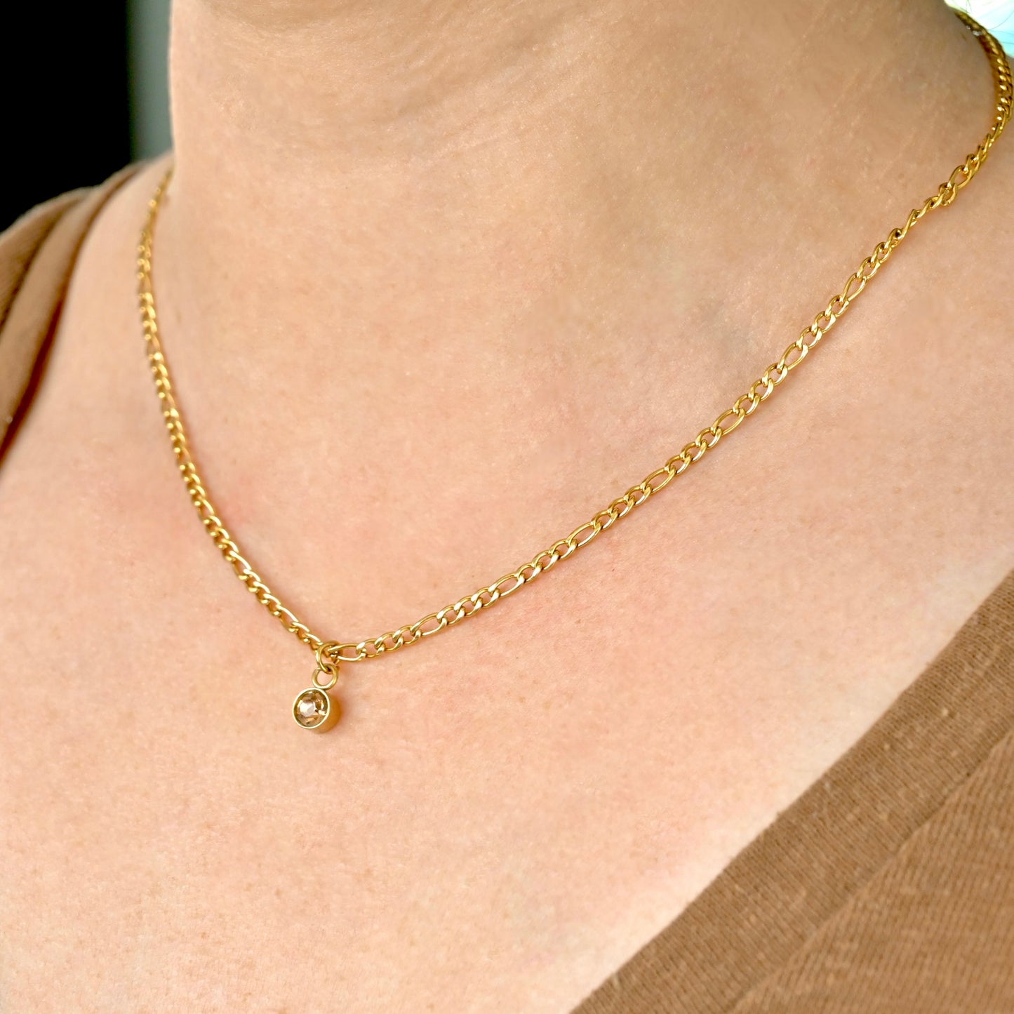 Gold  figaro necklace with round november birthstone on a person's neck