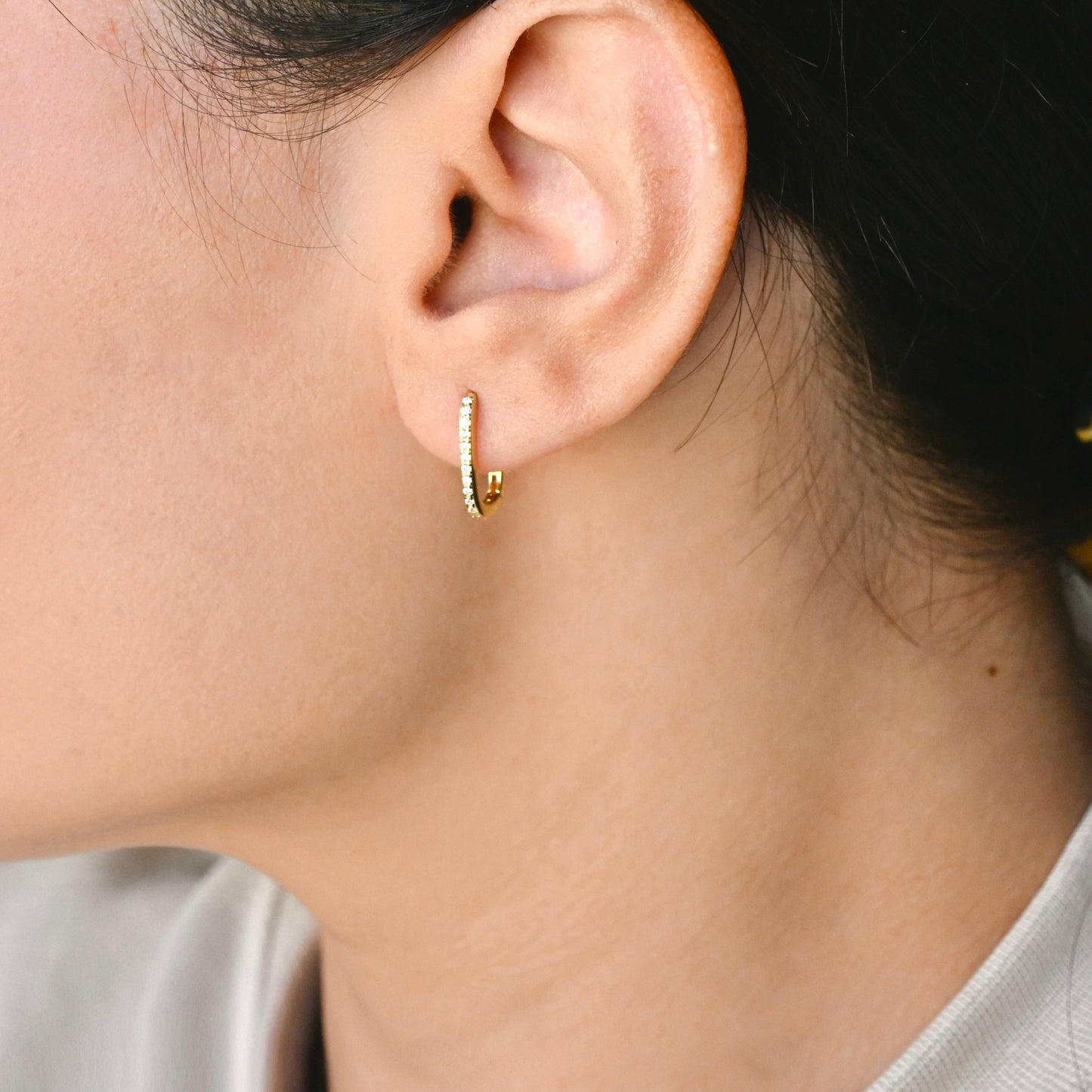 Close-up of an ear wearing a rectangular pave hoop earring with a blurred background