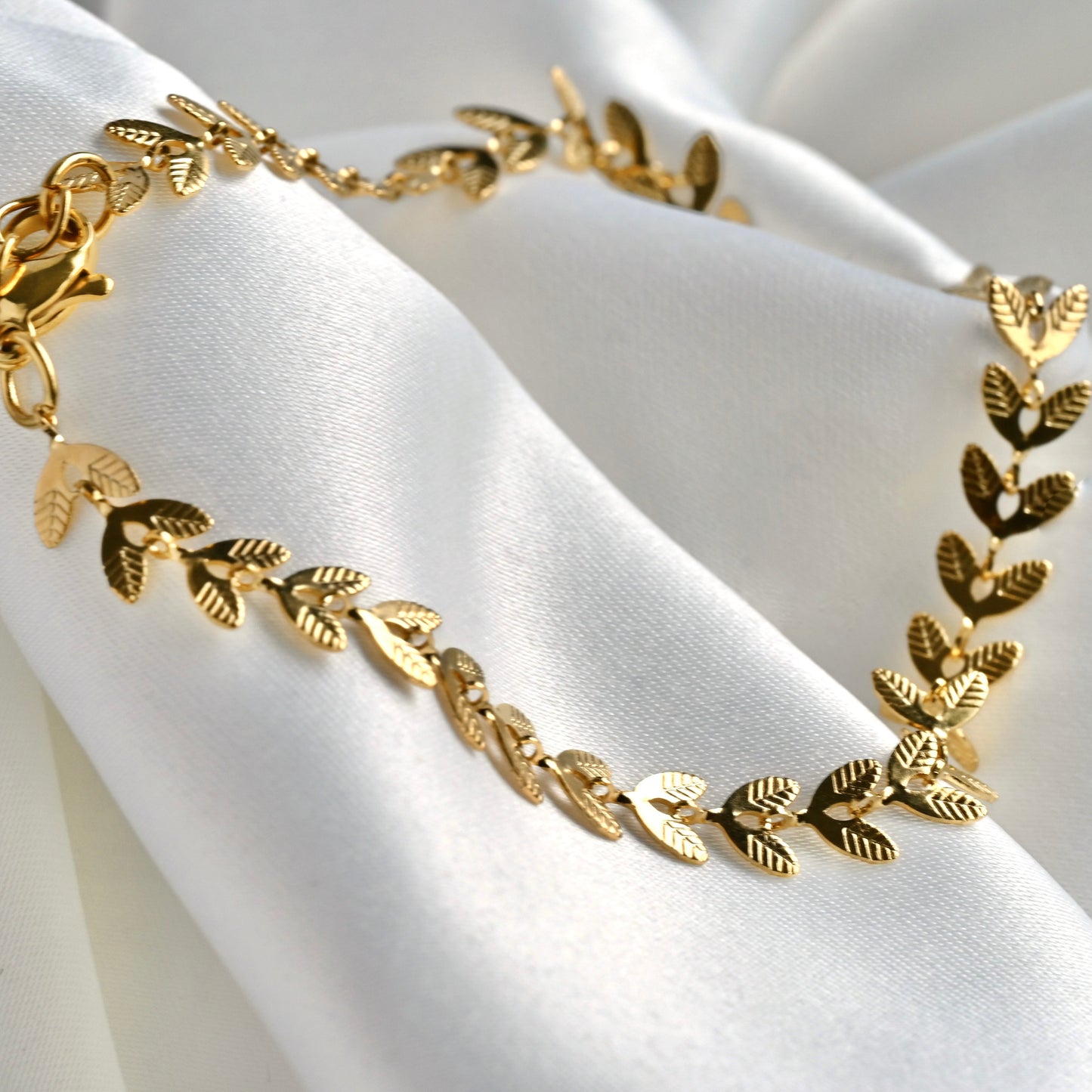 Gold bracelet with leaf designs on a white fabric background