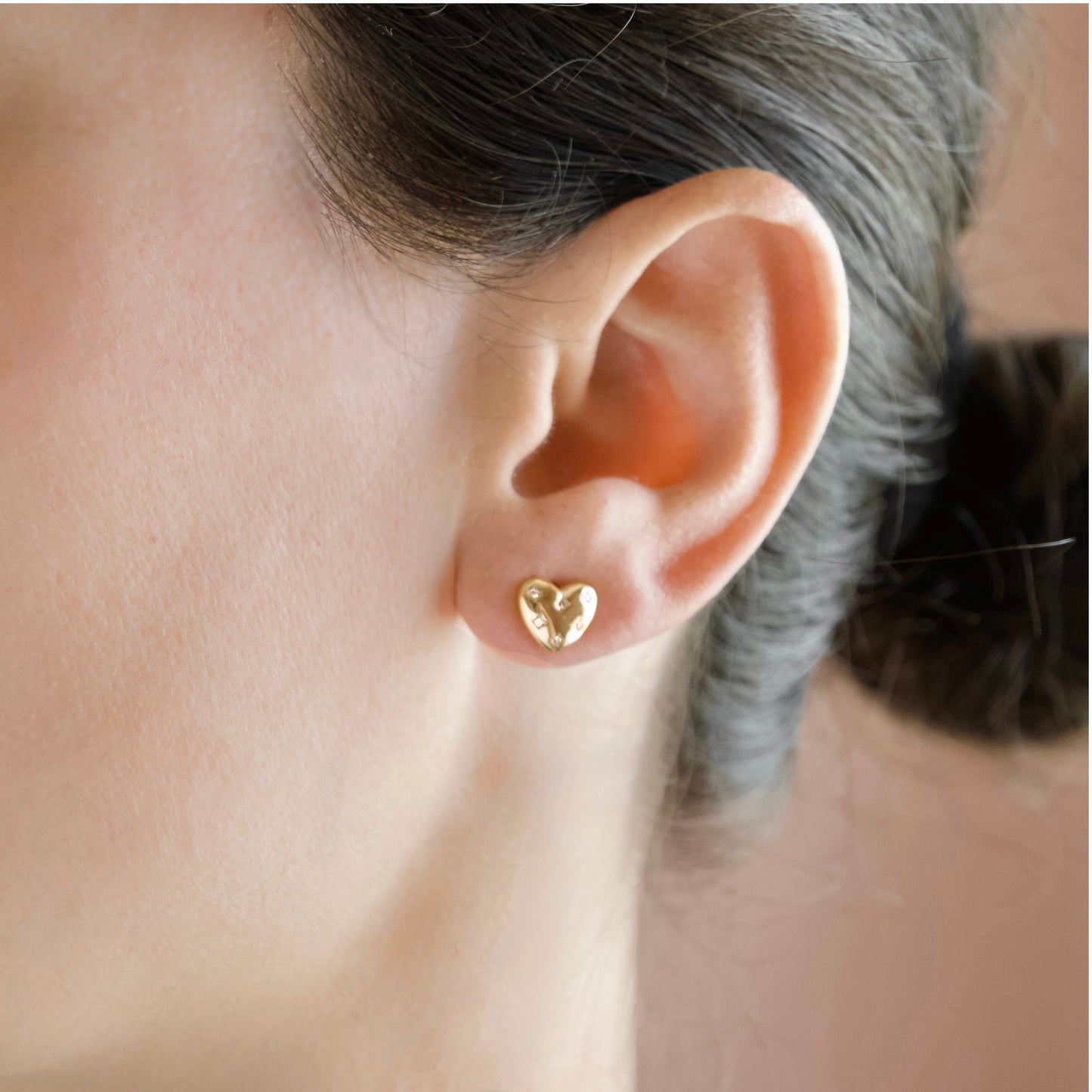 A close-up of a person's ear wearing a small gold heart-shaped stud earring.