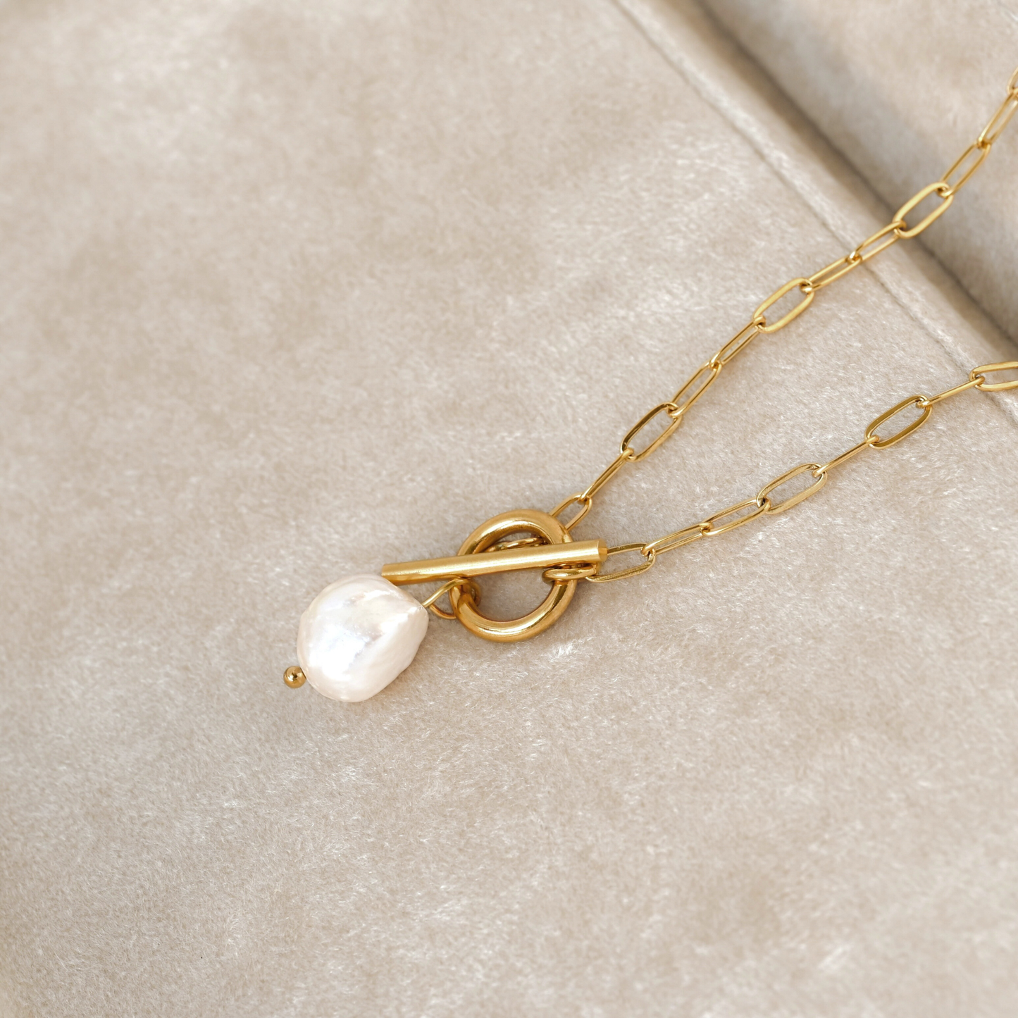 Gold necklace with a pearl pendant on a beige surface