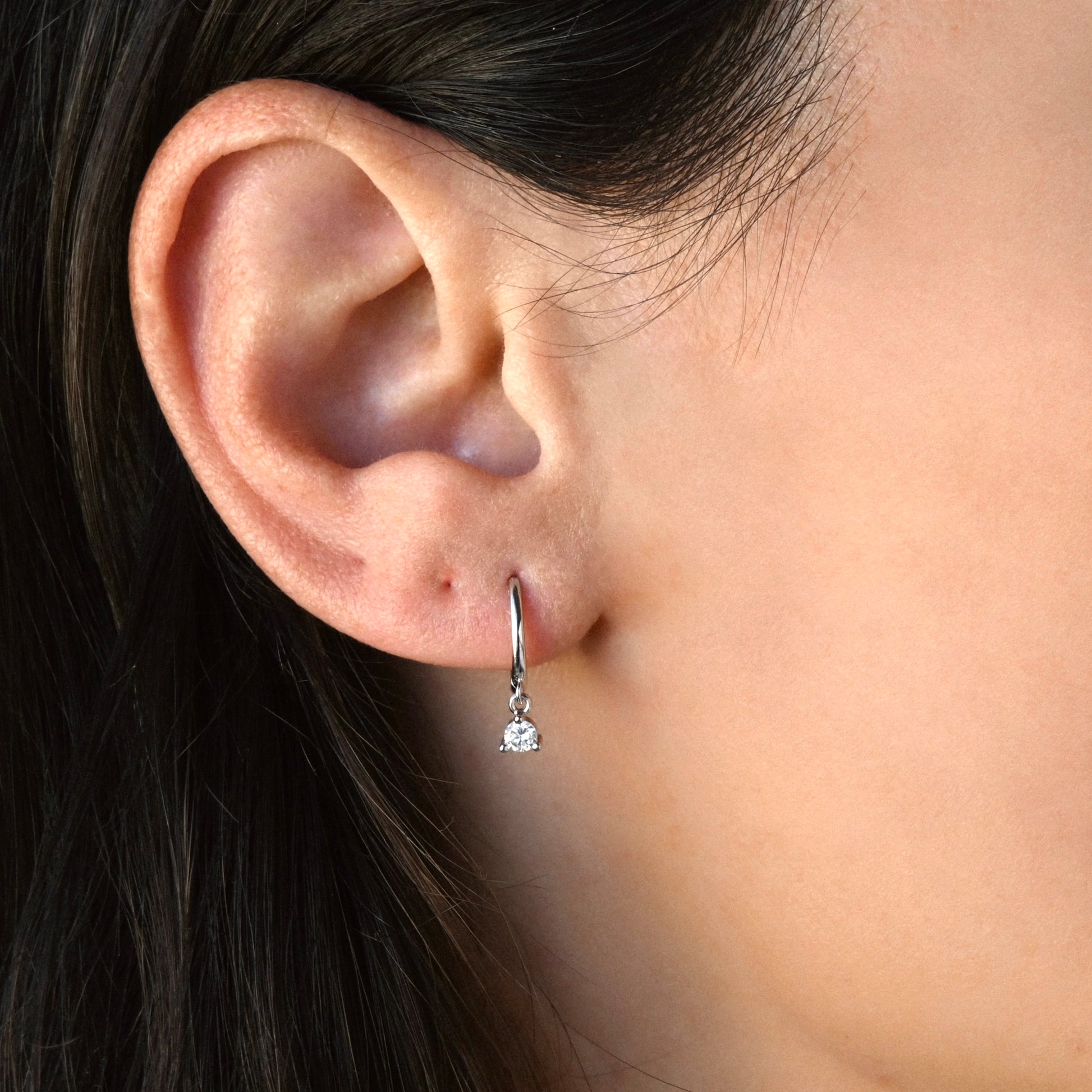 Close-up of a dark haired women wearing a silver finish diamond dangle earring.