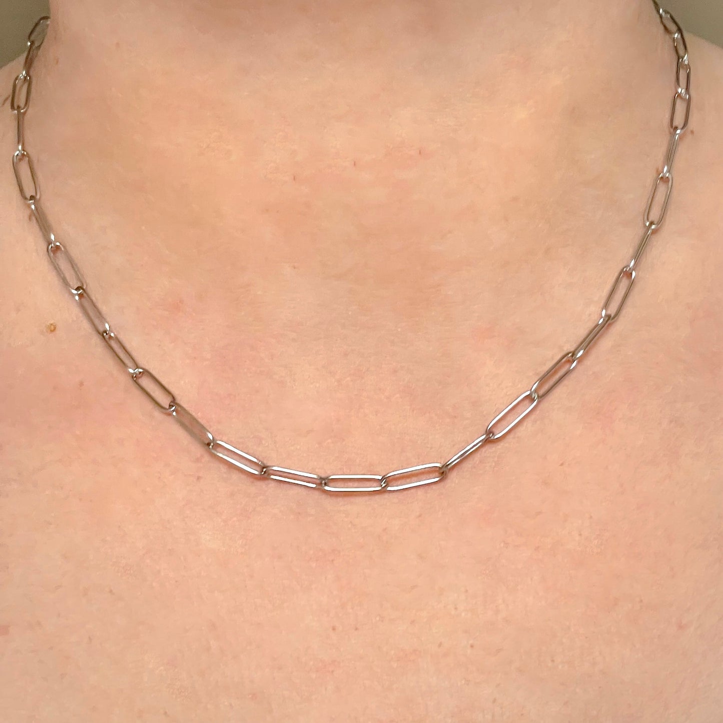 Silver paperclip link necklace on a person's neck against a neutral background
