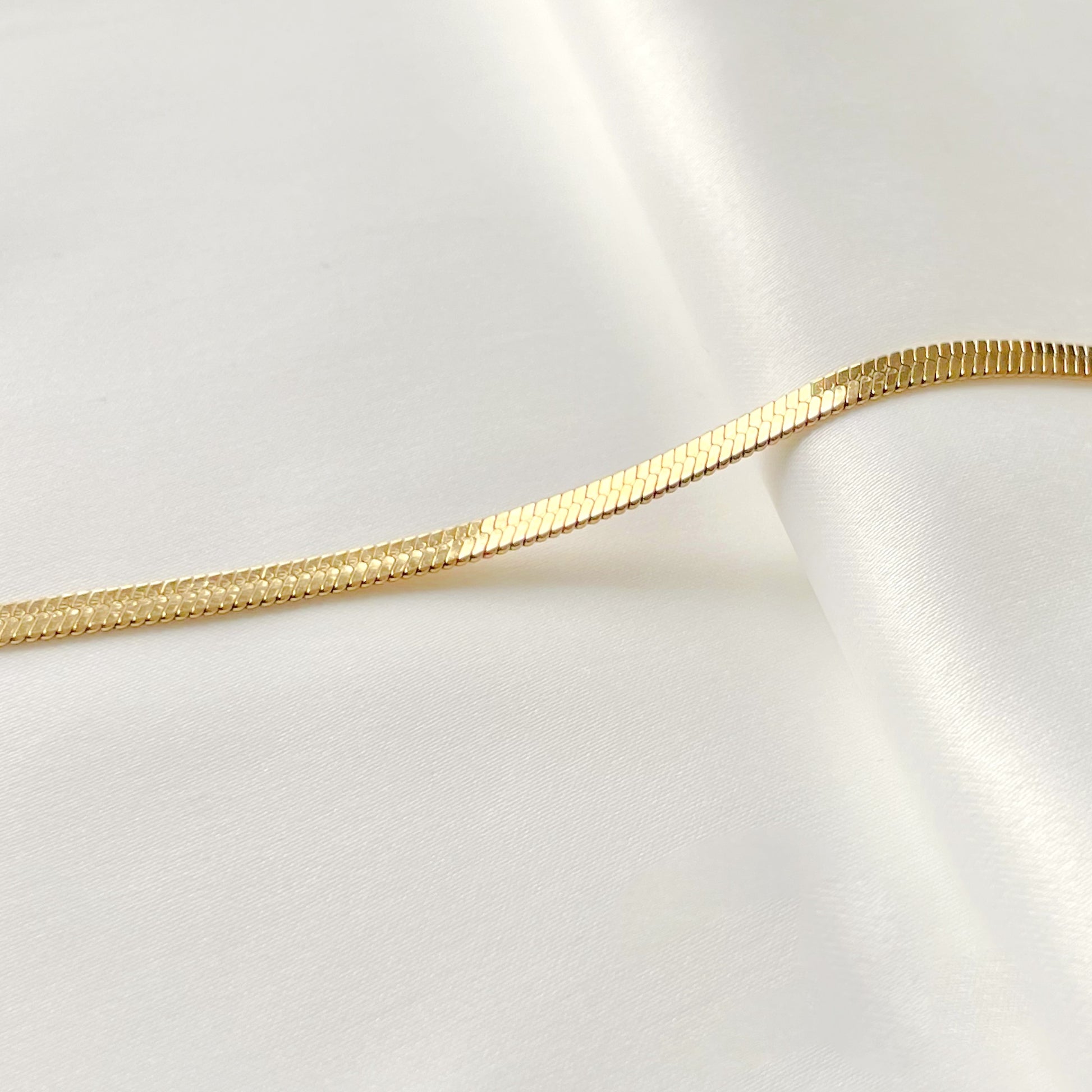 Gold herringbone chain on a white fabric background