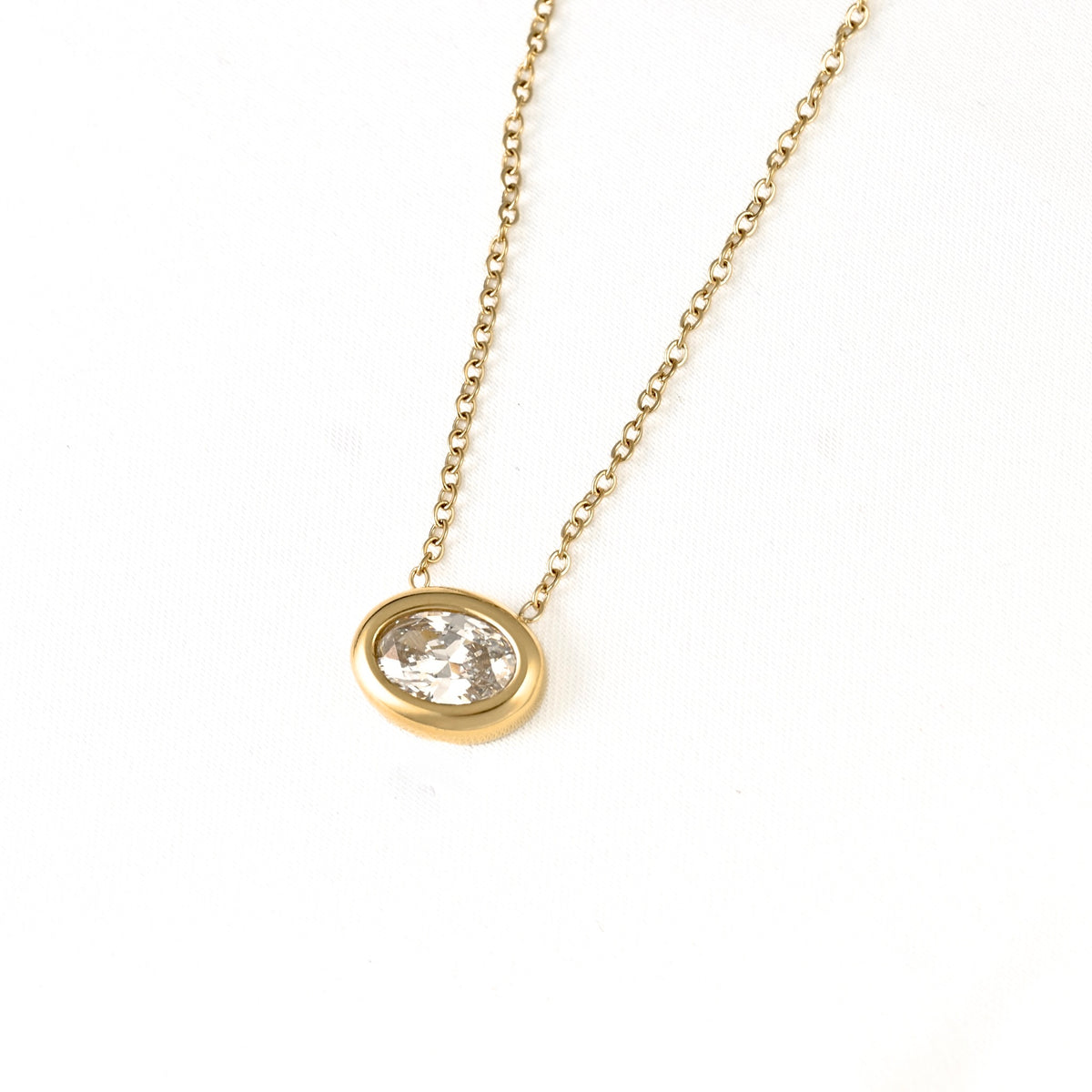 A gold chain necklace with an oval bezel setting holding a clear faceted gemstone, photographed on a plain white background.