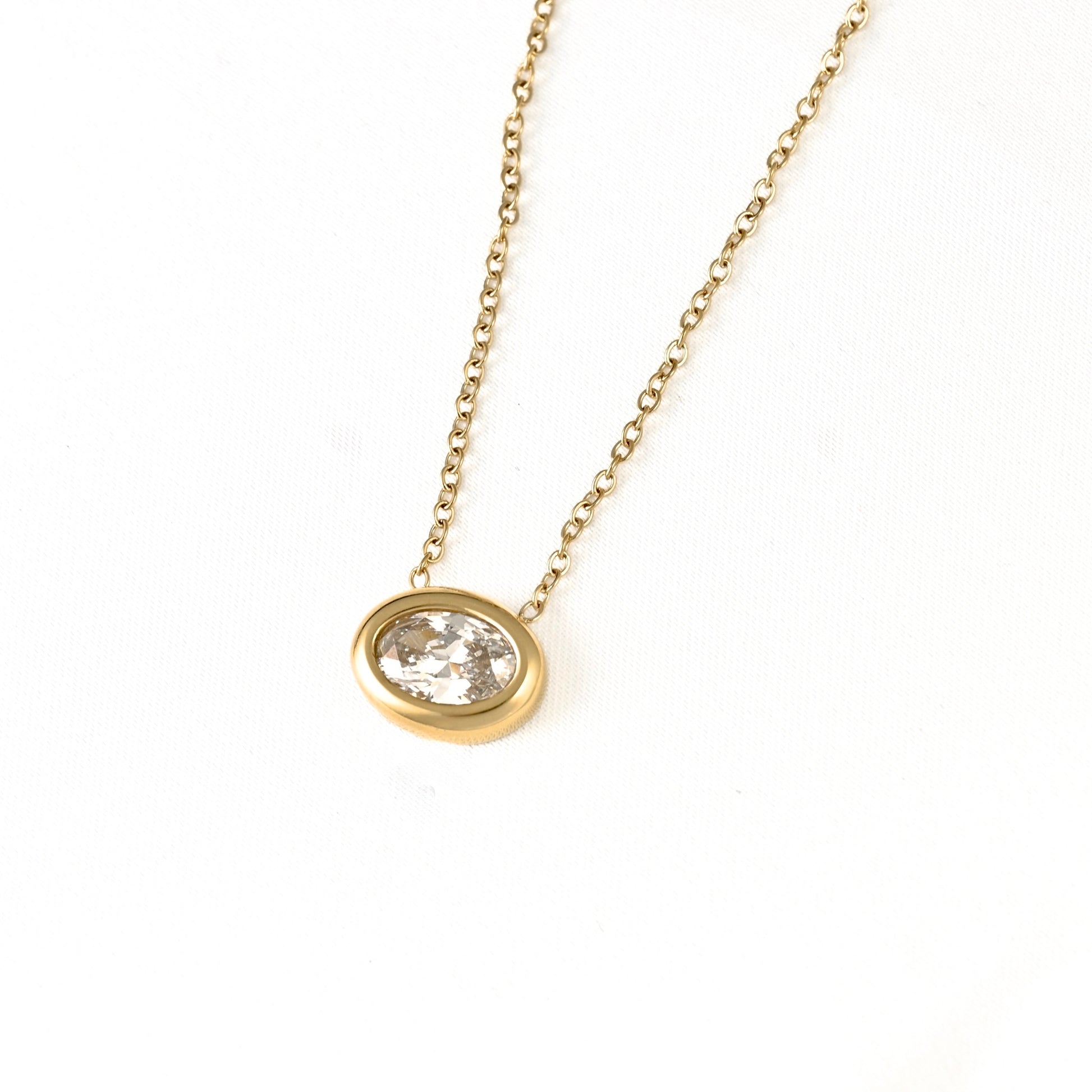 A gold chain necklace with an oval bezel setting holding a clear faceted gemstone, photographed on a plain white background.