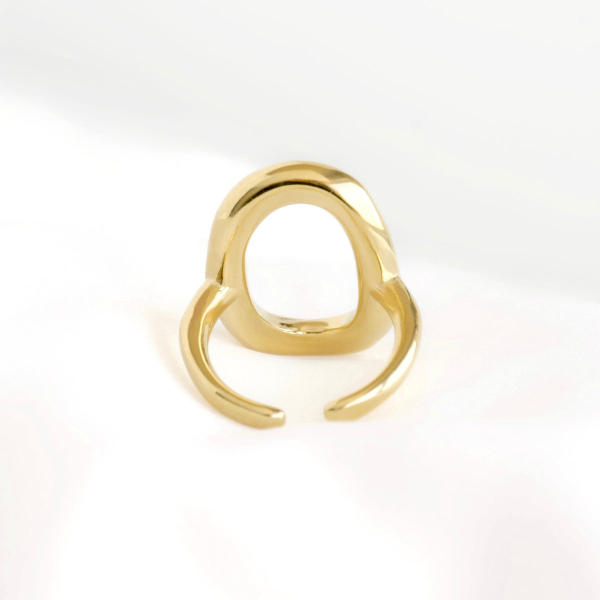 A polished gold-colored open ring with a curved, sculptural design, photographed on a clean white background.