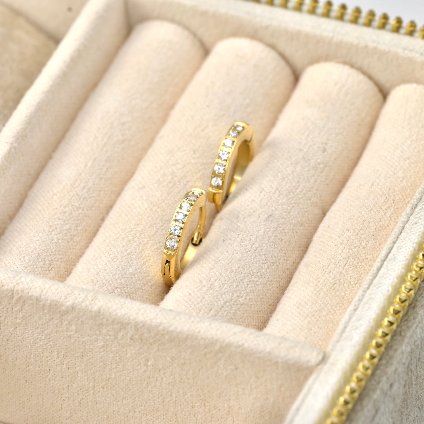 Gold diamond huggie earrings with clear stones on a beige jewelry display box.