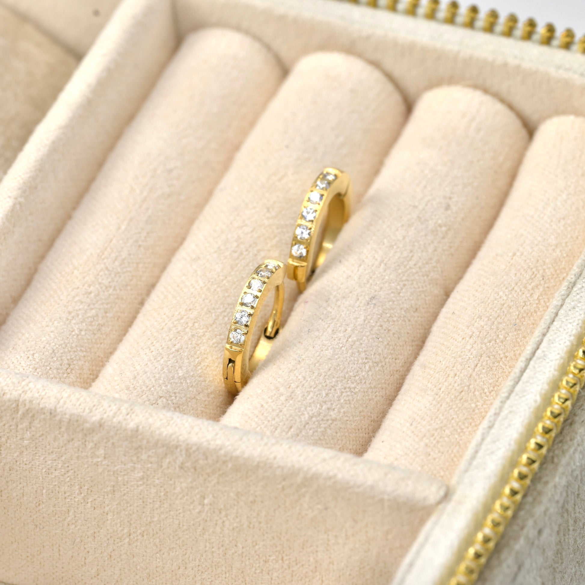 Gold diamond huggie earrings with clear stones on a beige jewelry display box.