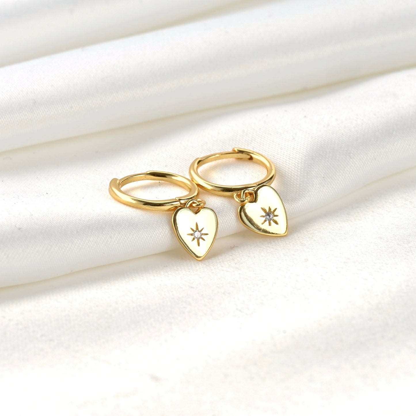 Gold huggie earings with CZ heart charm on a white fabric background