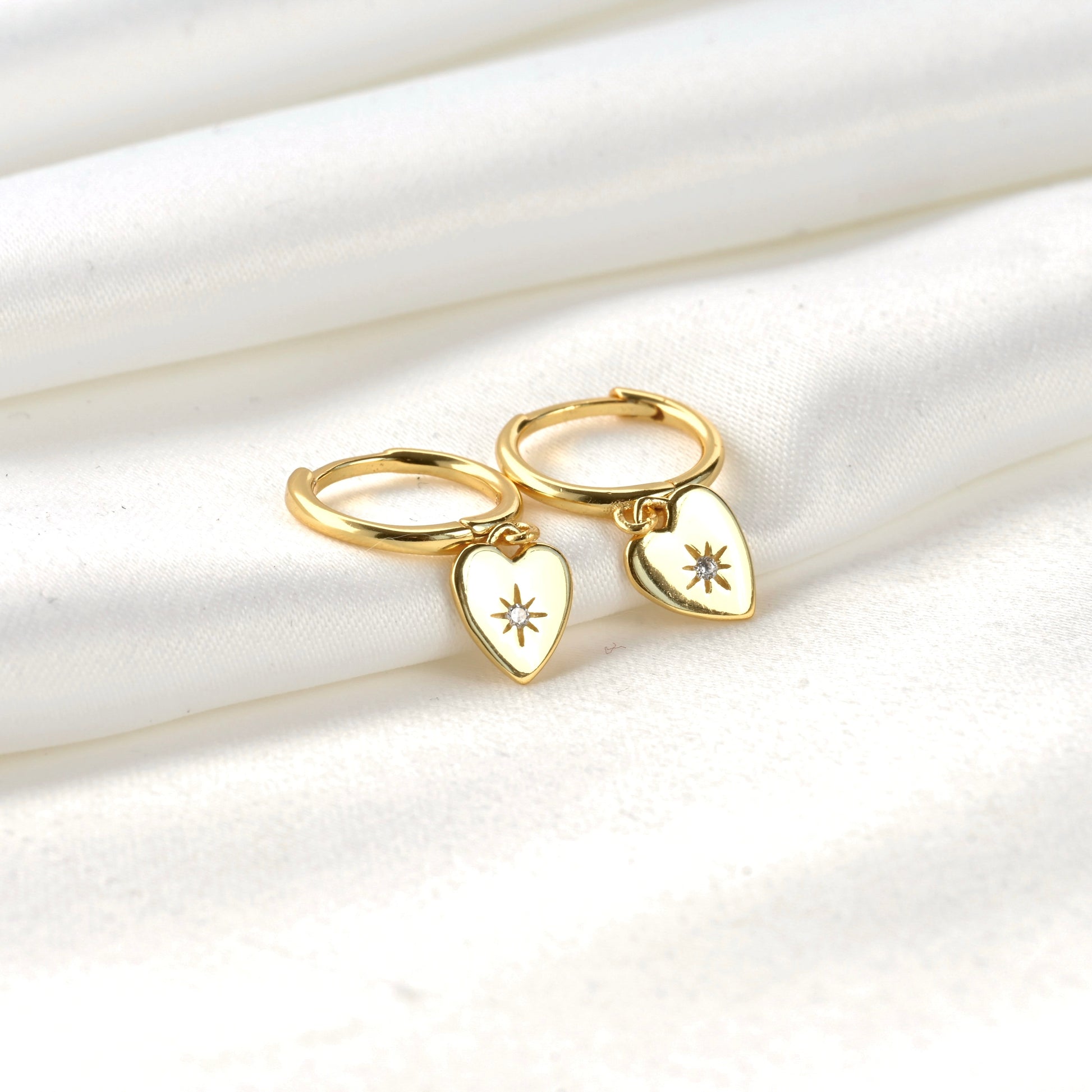 Gold huggie earings with CZ heart charm on a white fabric background