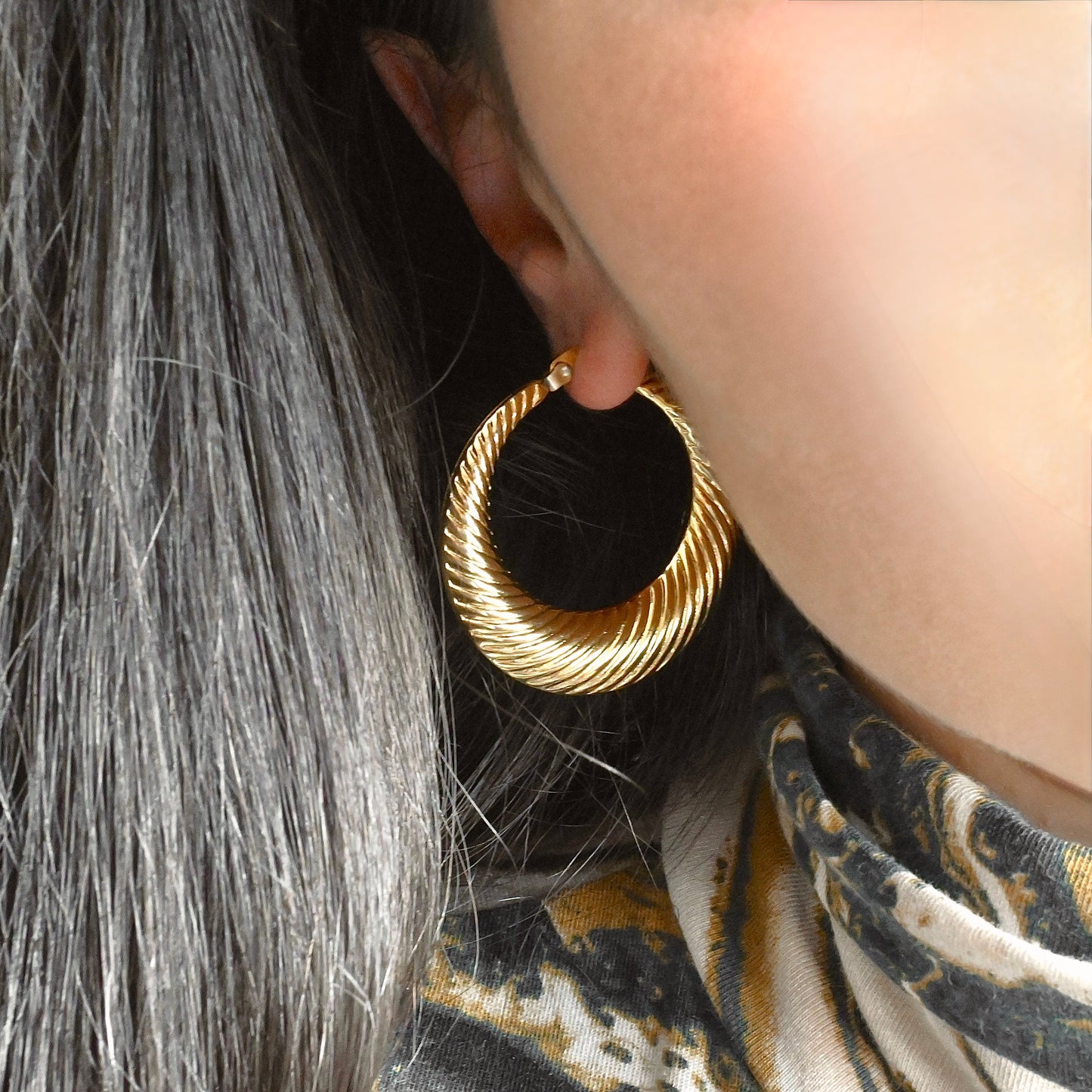 Close-up of a person wearing large gold croissant hoop earrings 