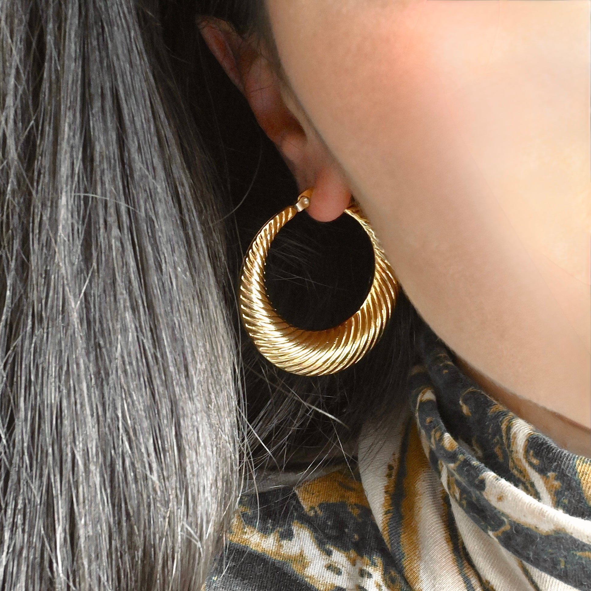 Close-up of a person wearing large gold croissant hoop earrings 
