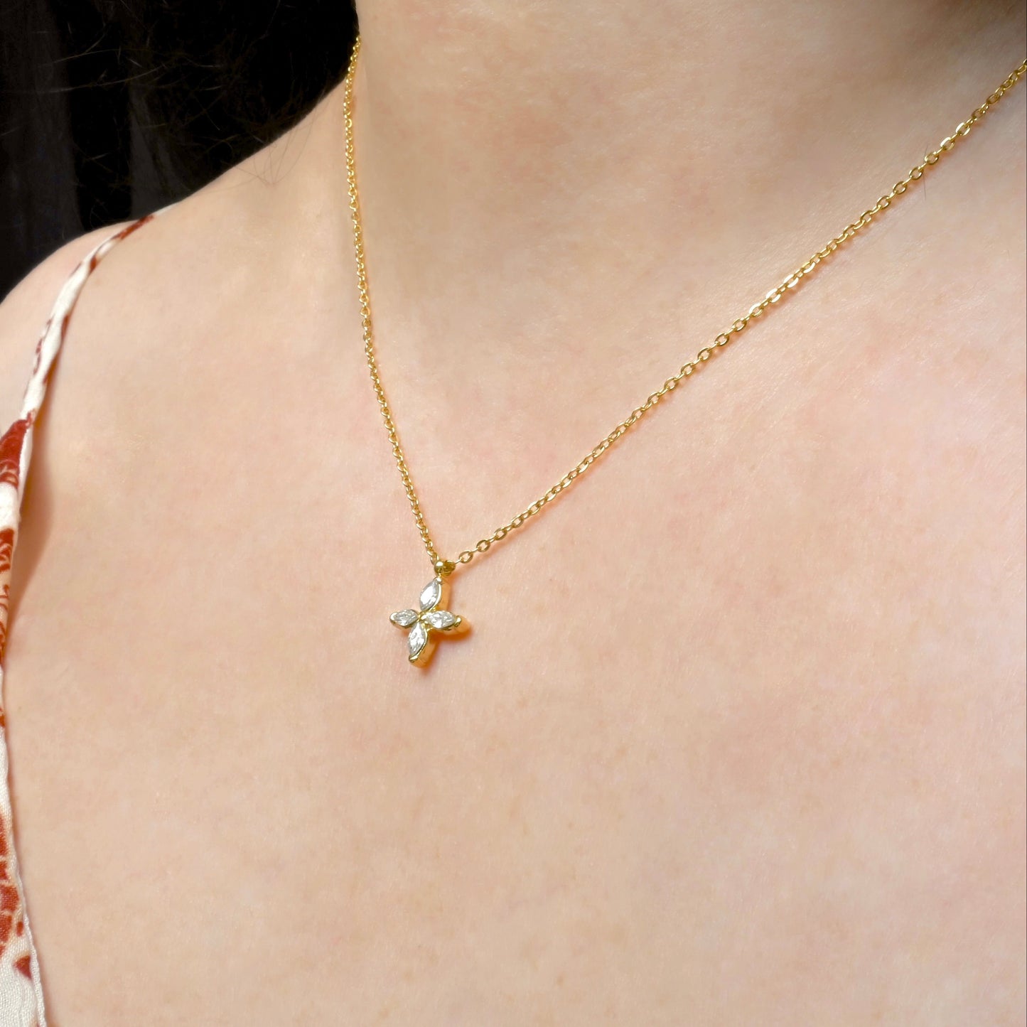 Gold flower pendant necklace with marquise-cut stone inlays on a person wearing a patterned top.