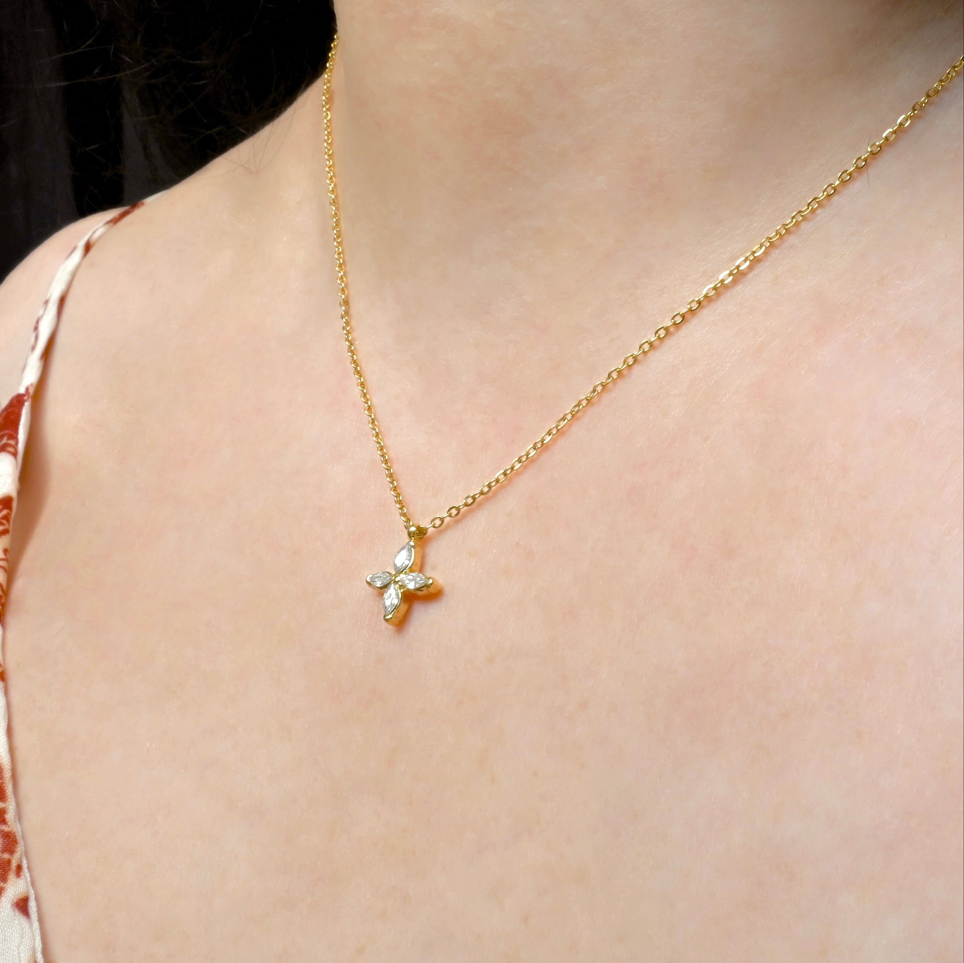 Gold flower pendant necklace with marquise-cut stone inlays on a person wearing a patterned top.