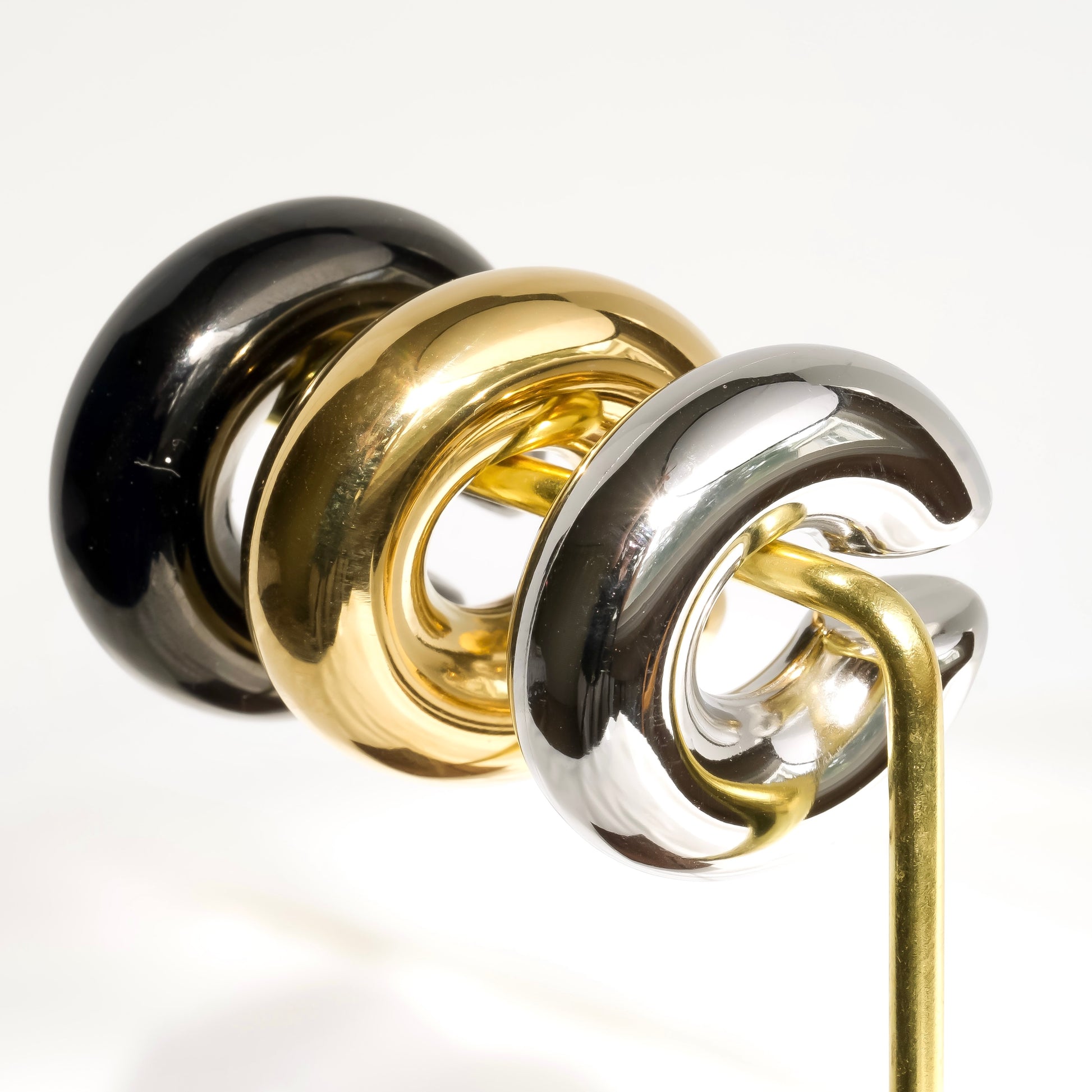 Three hoop earrings in black, gold, and silver on an earring stand