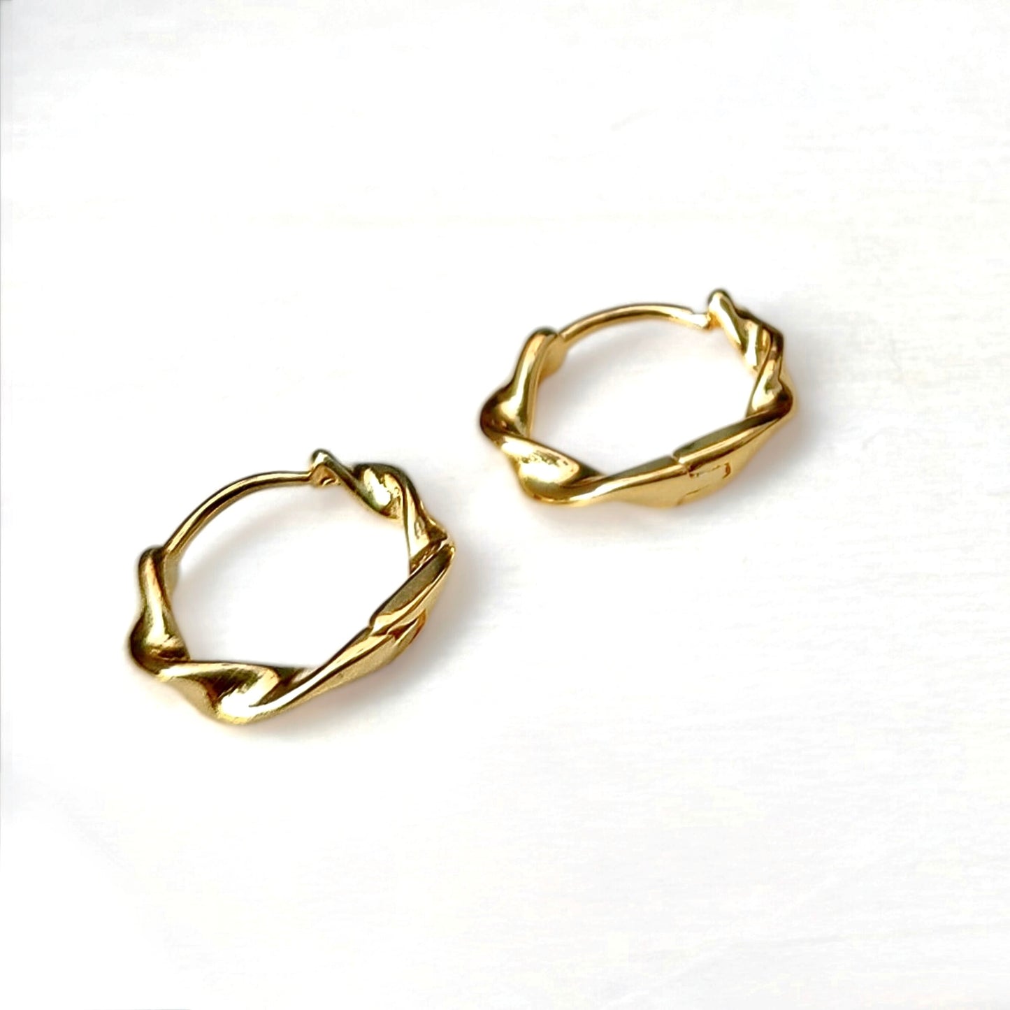 Small gold twirling hoop earrings on a white background