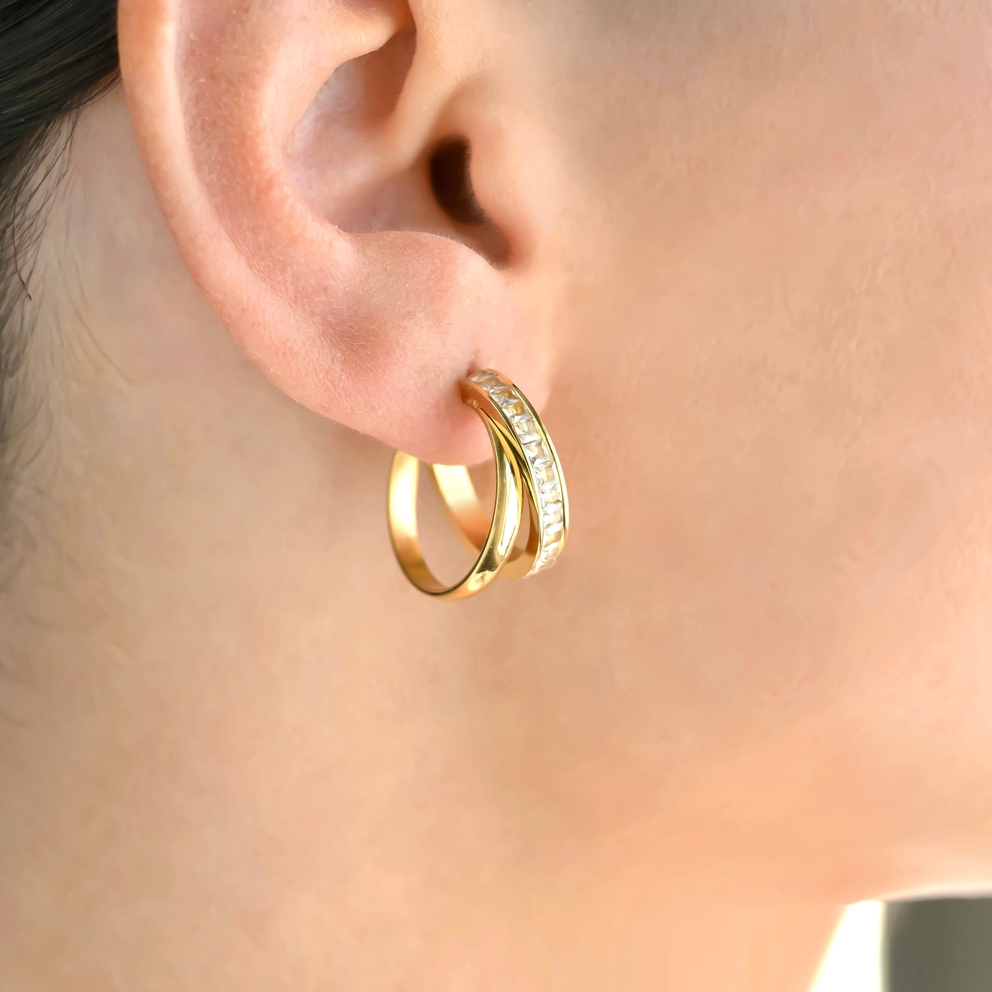 Gold layered mixed hoop earrings with embedded stones worn by a person.