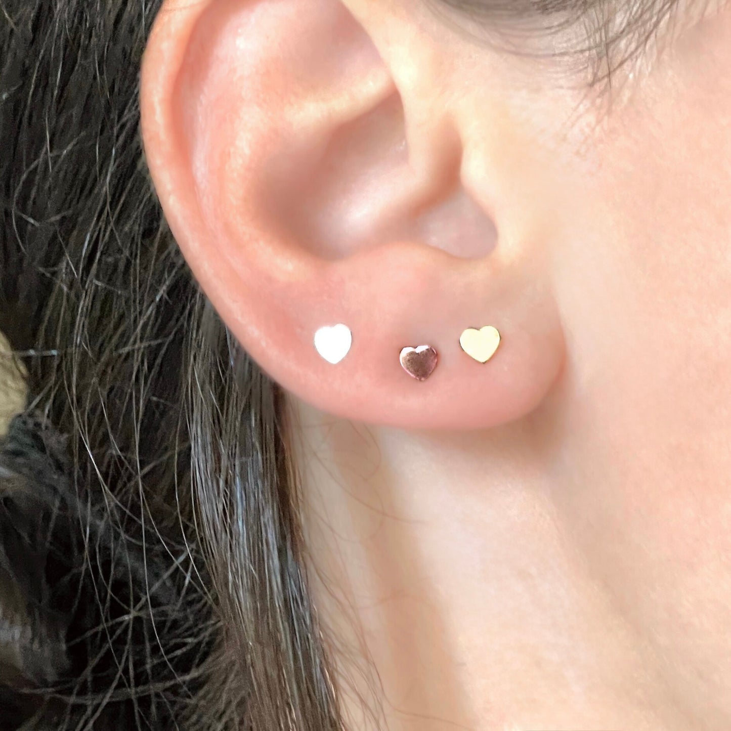 Close-up of an ear wearing three heart-shaped earrings.